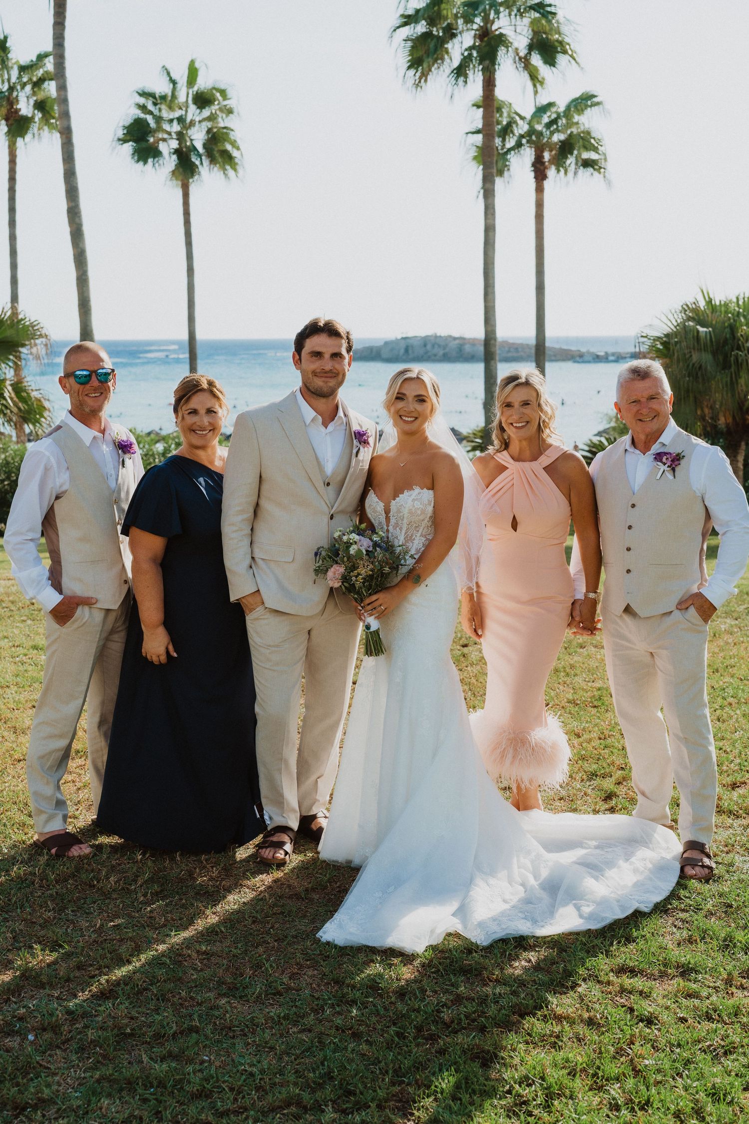 Wedding party in white and cream attire gather for group photos at oceanfront venue.