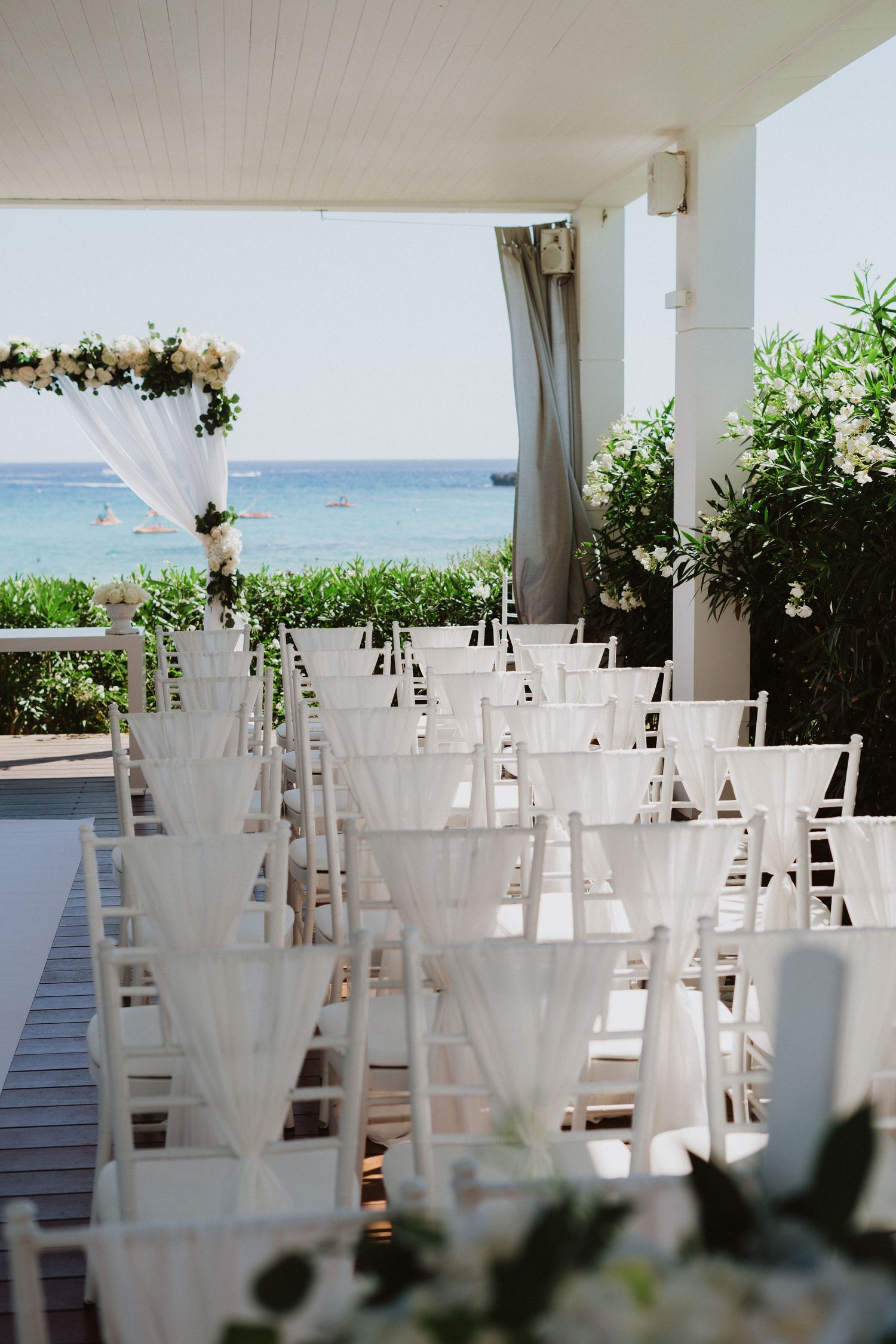 White chairs arranged for an oceanfront wedding ceremony with floral decorations.