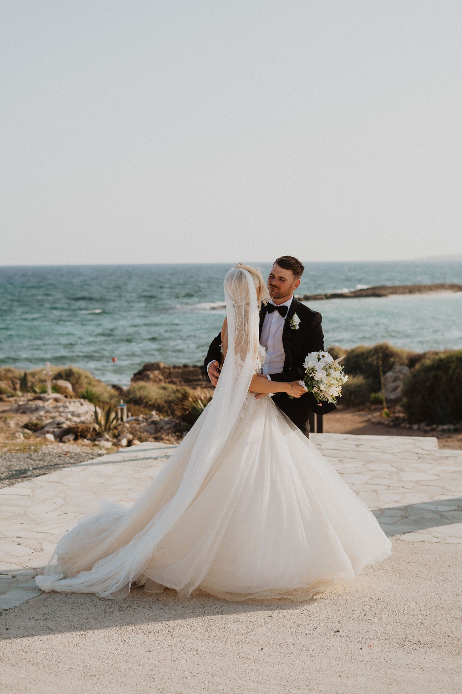 Elegant couple poses for wedding photos against blue ocean backdrop.