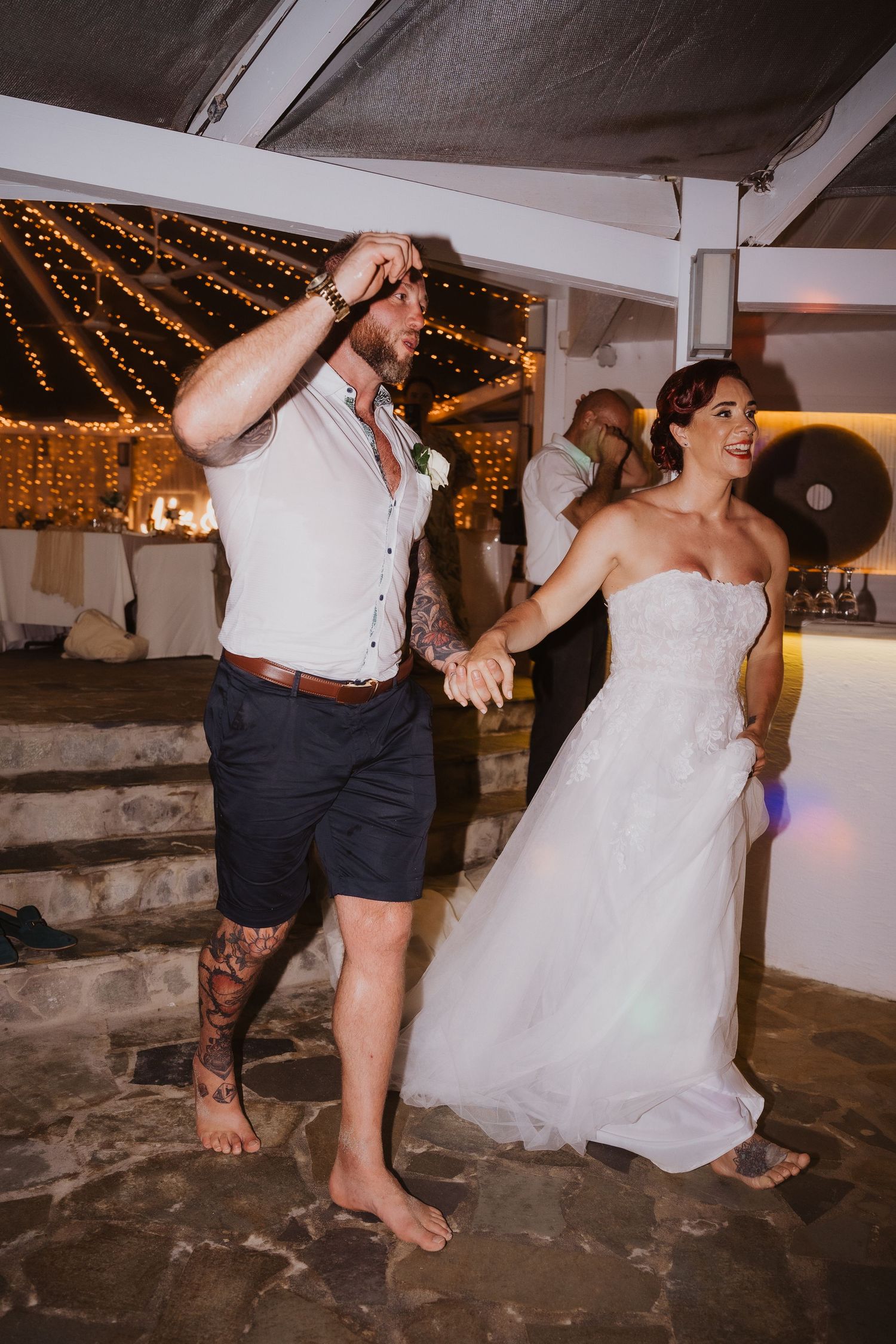 Barefoot couple dancing at a wedding reception under string lights.