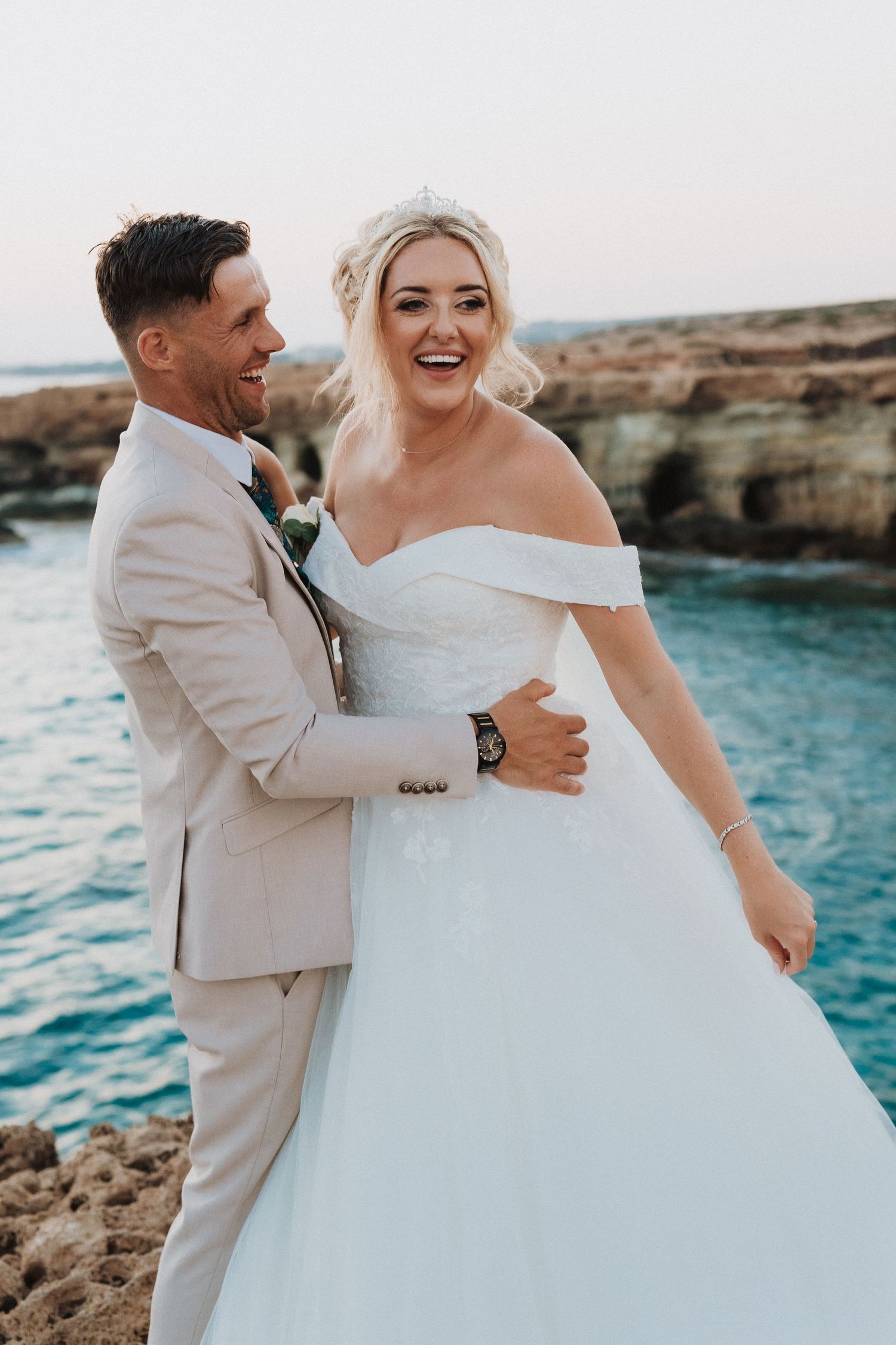 A happy couple celebrates their wedding day by a scenic ocean cliff with bright turquoise water in the background.