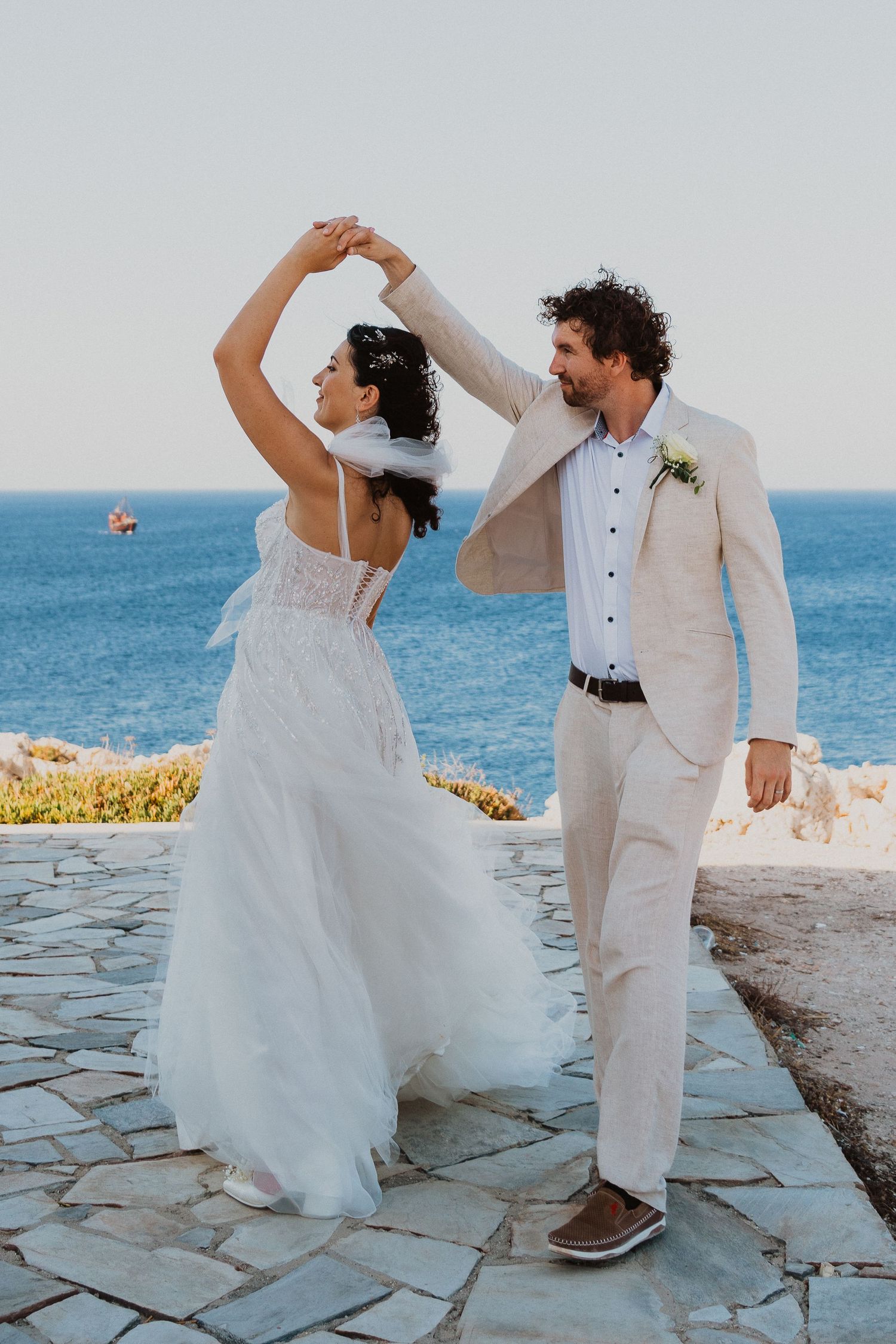 Couple dancing on stone terrace overlooking Mediterranean Sea during wedding celebration.