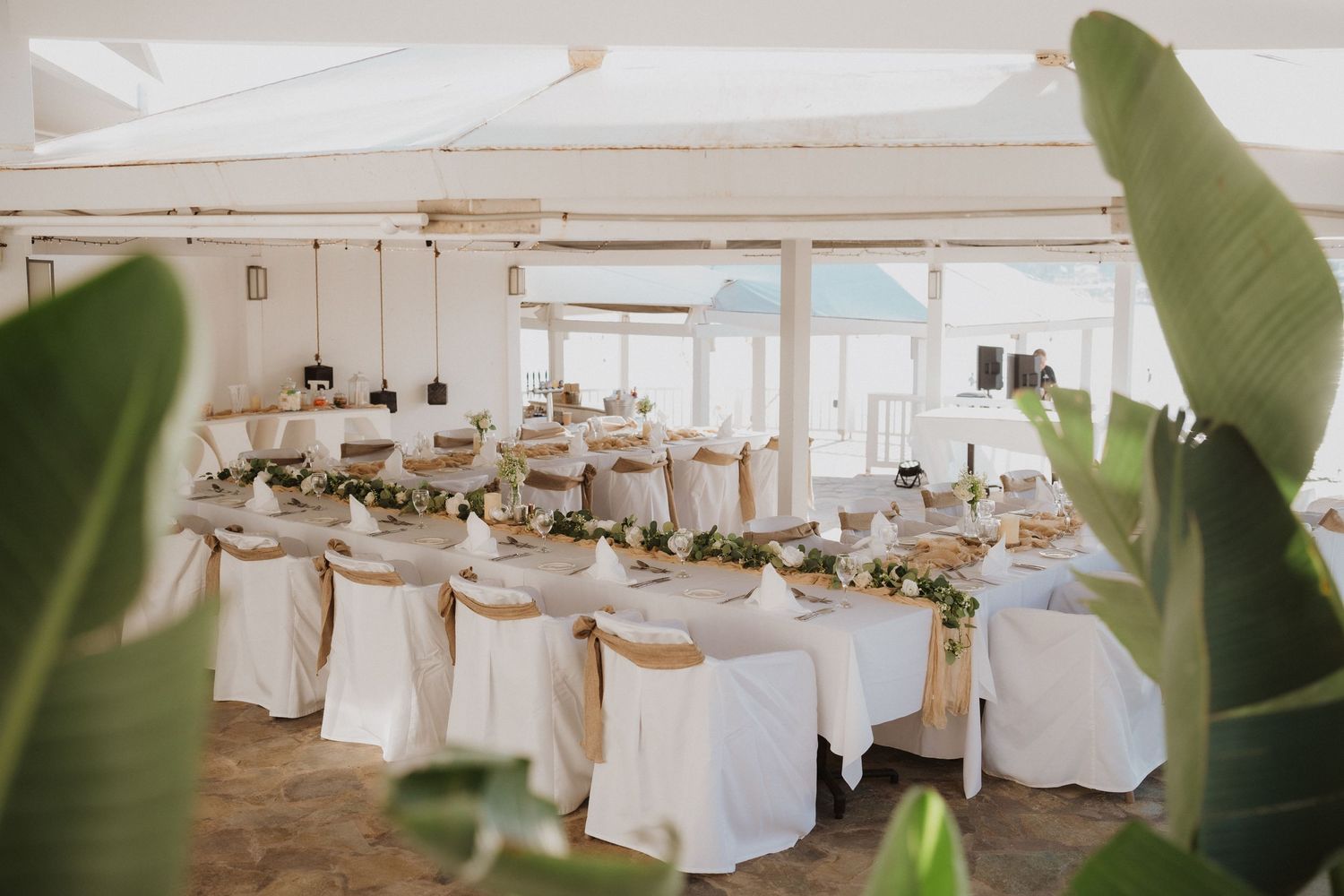 Elegant wedding reception setup with white-covered chairs and tropical decor.