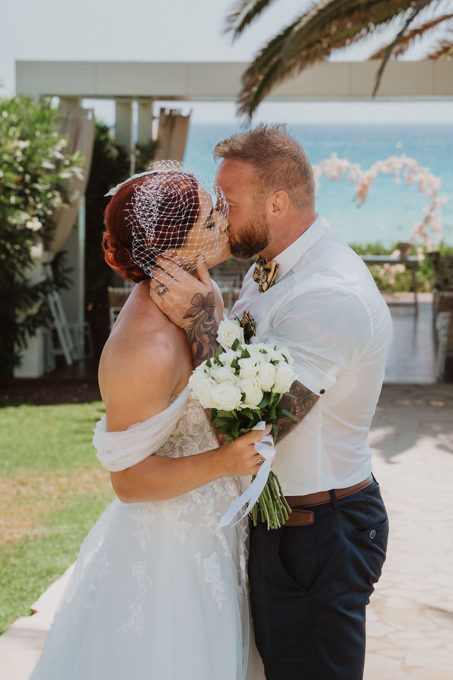 Close-up of wedding couple sharing intimate moment with ocean and palm trees in background.