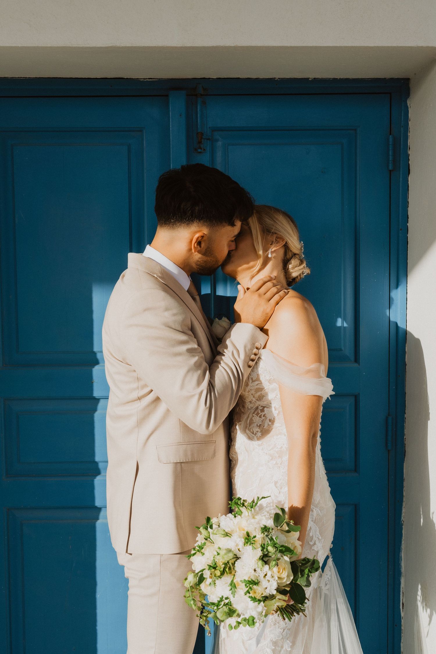 A tender wedding moment captured against bright blue doors with white flowers in hand.