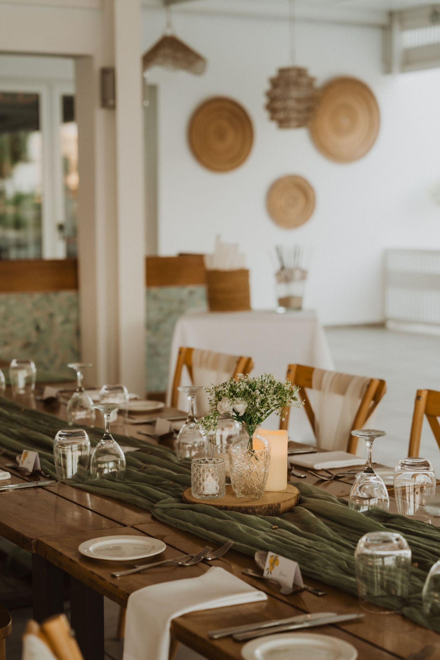Rustic wedding table setting with wooden decor, glass cloches, and decorative woven baskets on white walls.