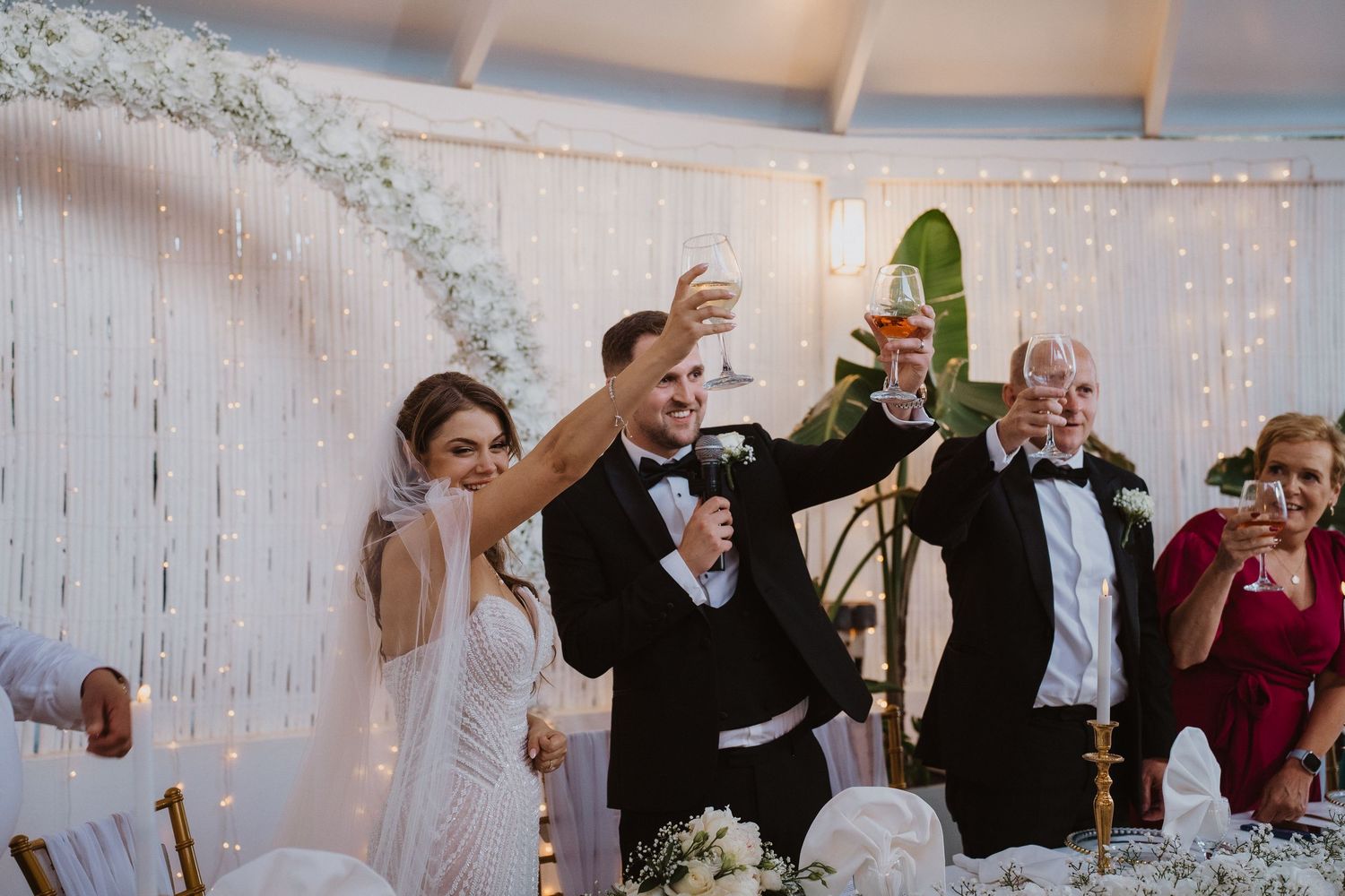 Bride and groom toasting with champagne during wedding reception under elegant fairy light decor.