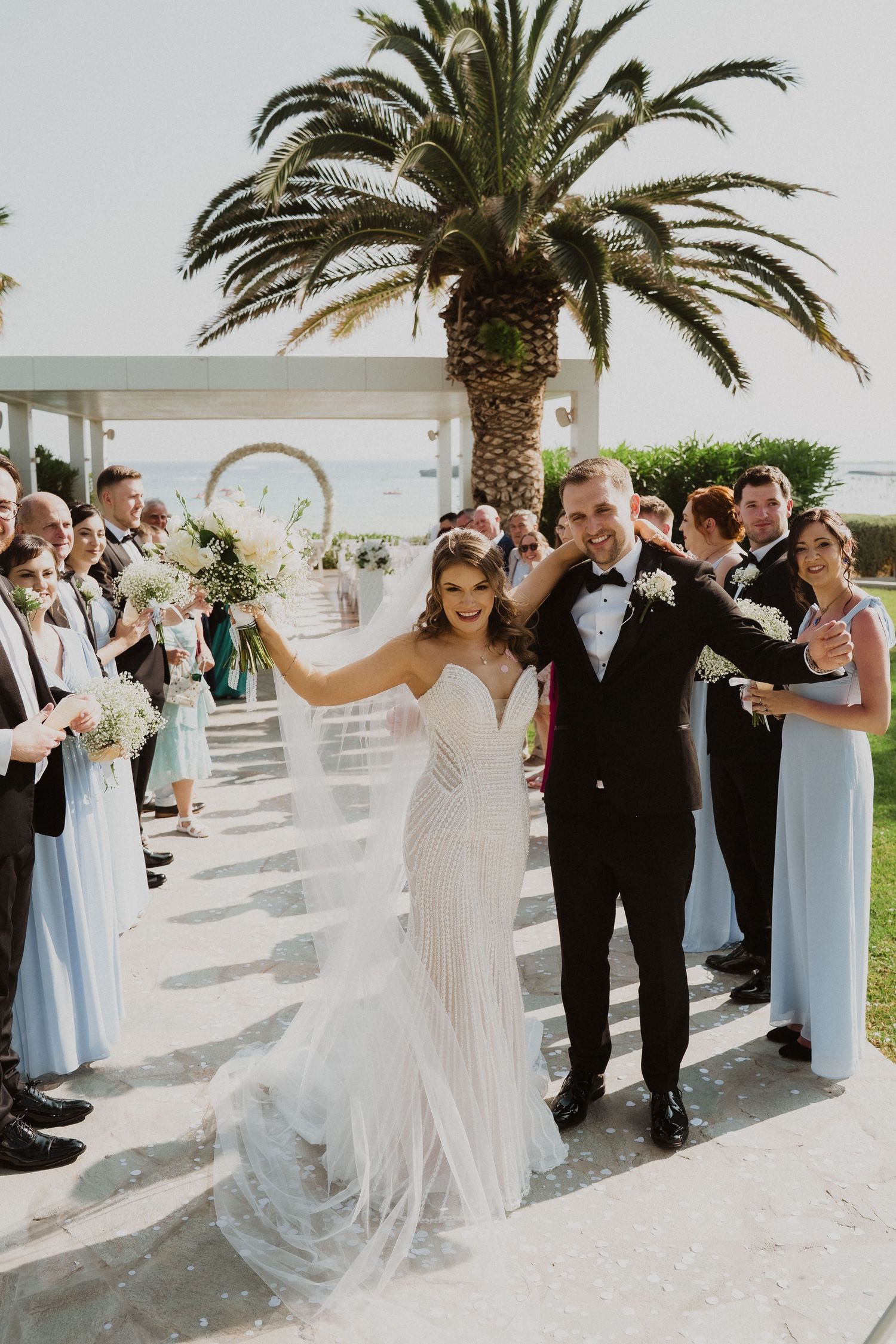 Bride and groom celebrate recessional with raised arms at stunning outdoor coastal wedding venue.