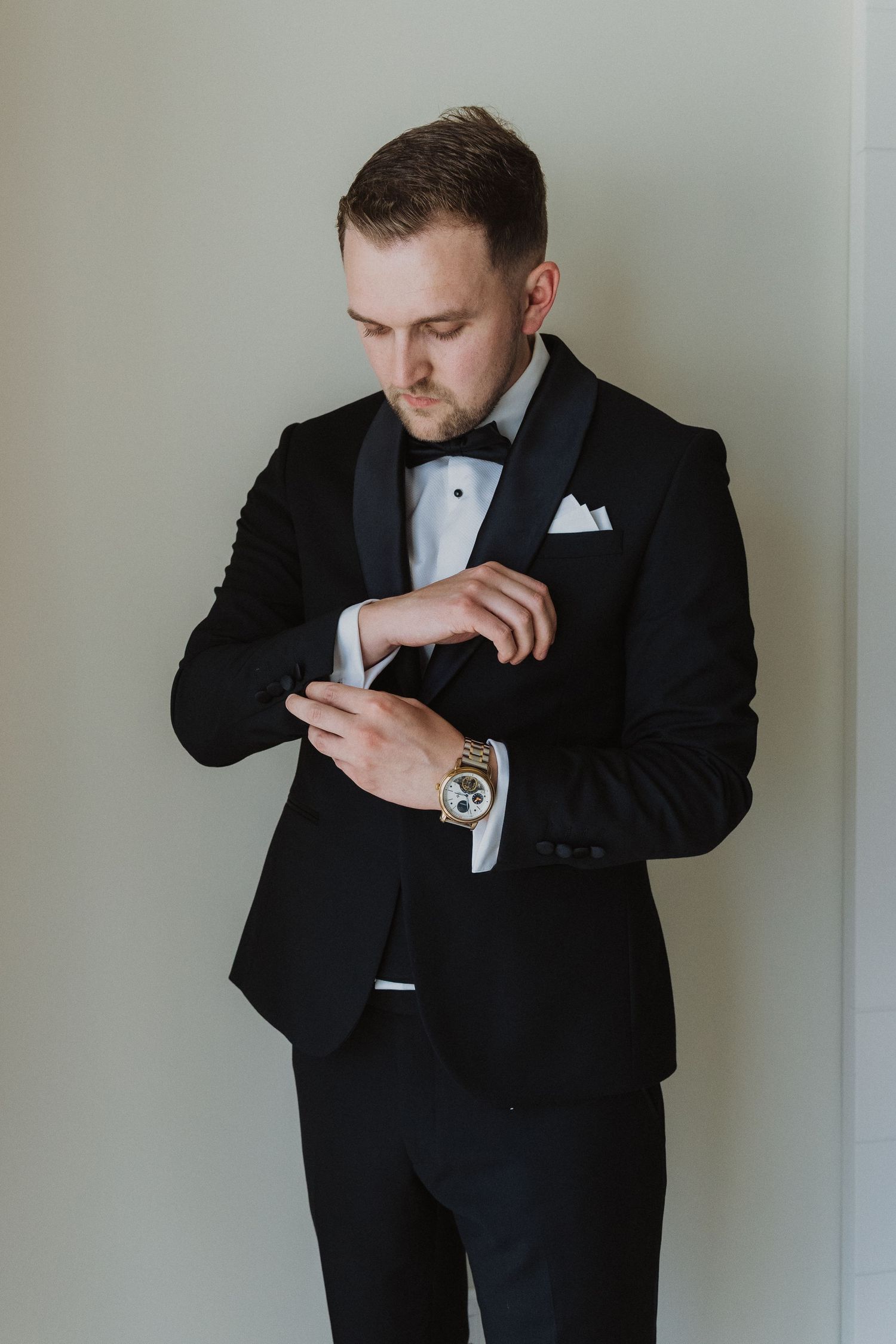 Elegant groom in black tuxedo adjusting cufflinks before wedding ceremony.