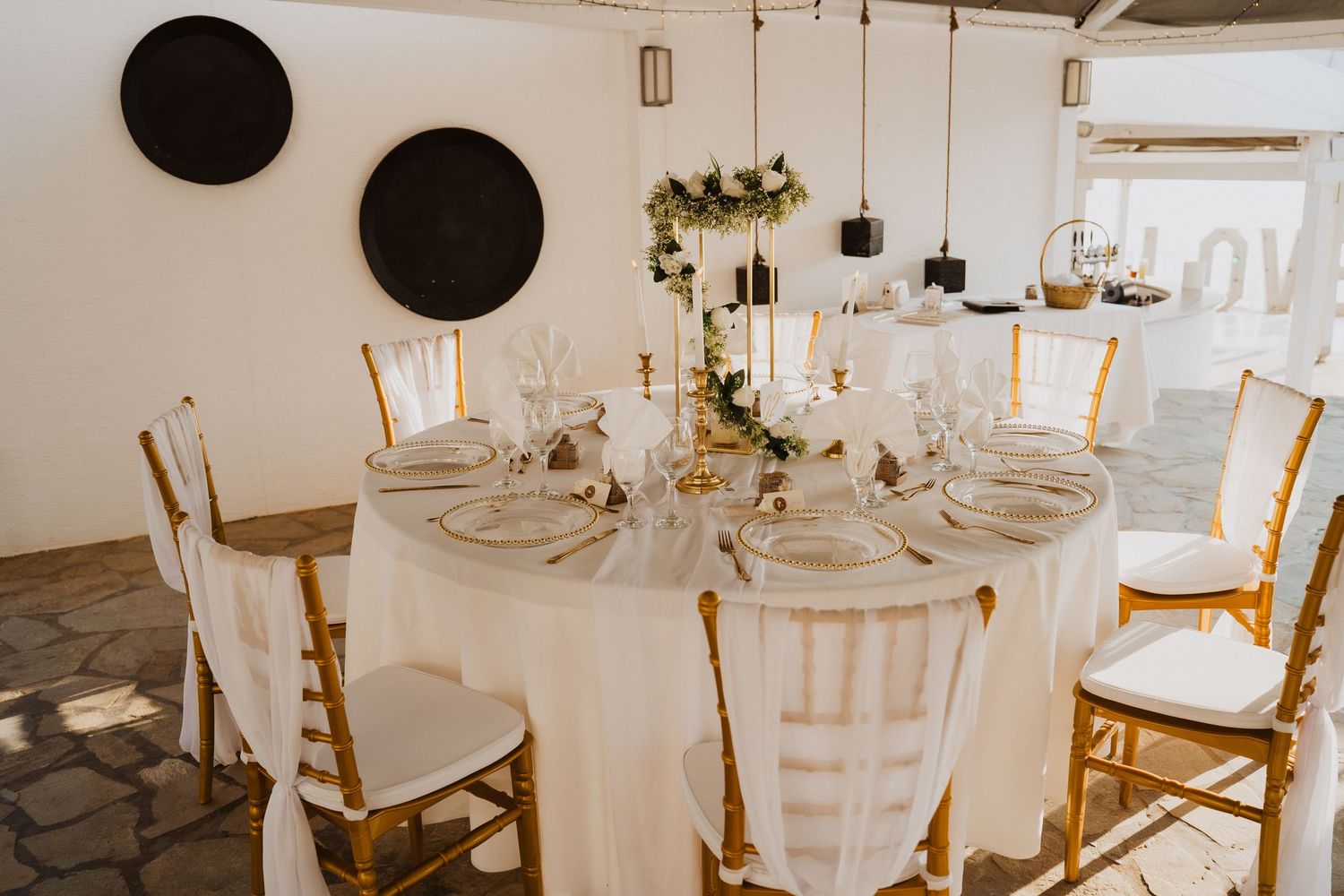 Elegant wedding reception table set with gold chiavari chairs, white linens, and greenery centerpiece.