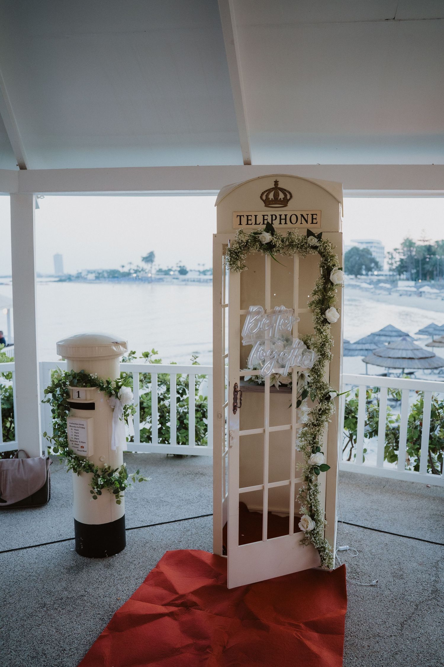 White vintage telephone booth decorated with greenery and floral garland at waterfront wedding venue.