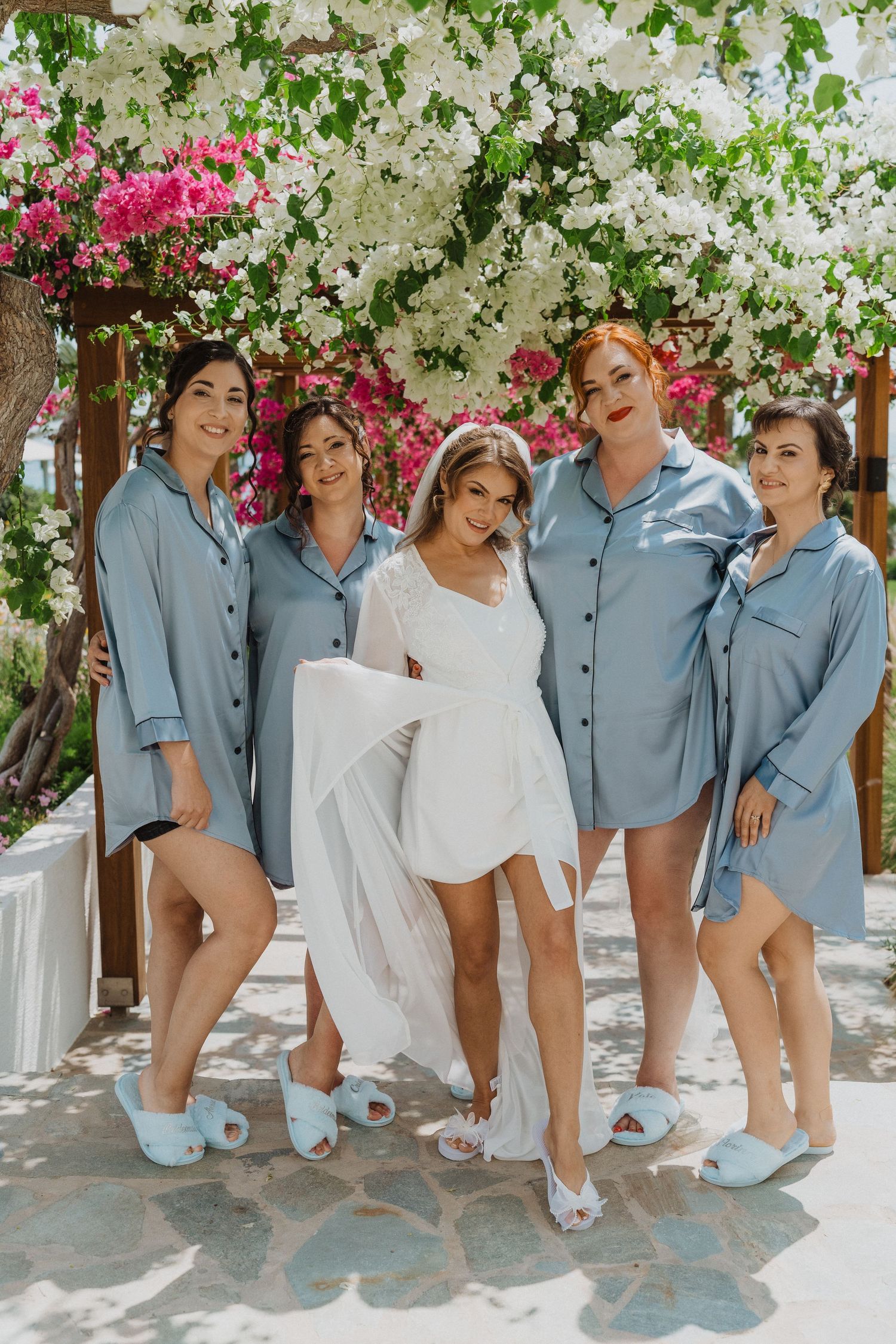 Bride and bridesmaids in matching blue shirts and slippers under flowers.