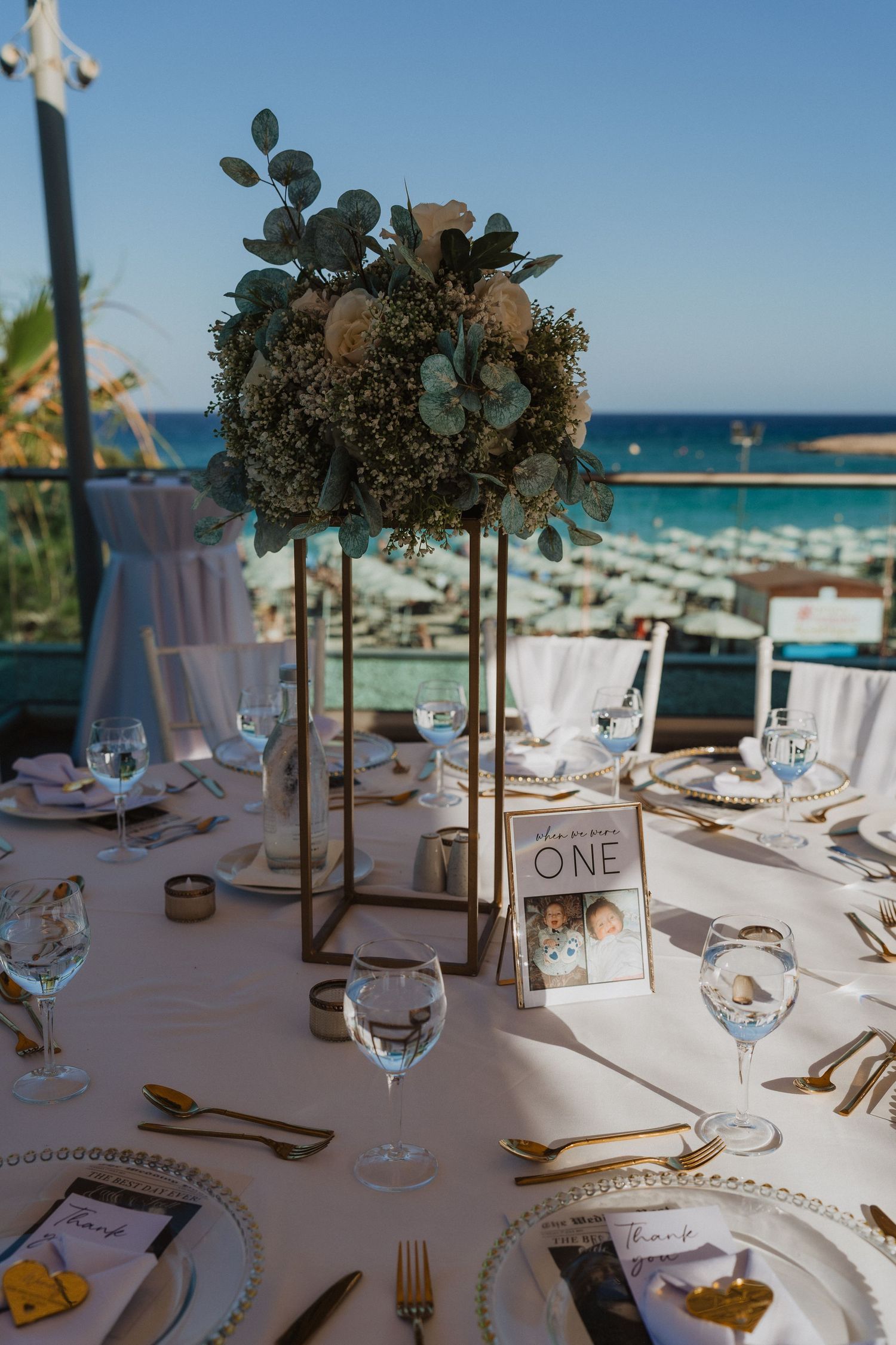 Elegant beach wedding reception tables with white linens, gold cutlery and floral centerpieces overlooking the ocean.