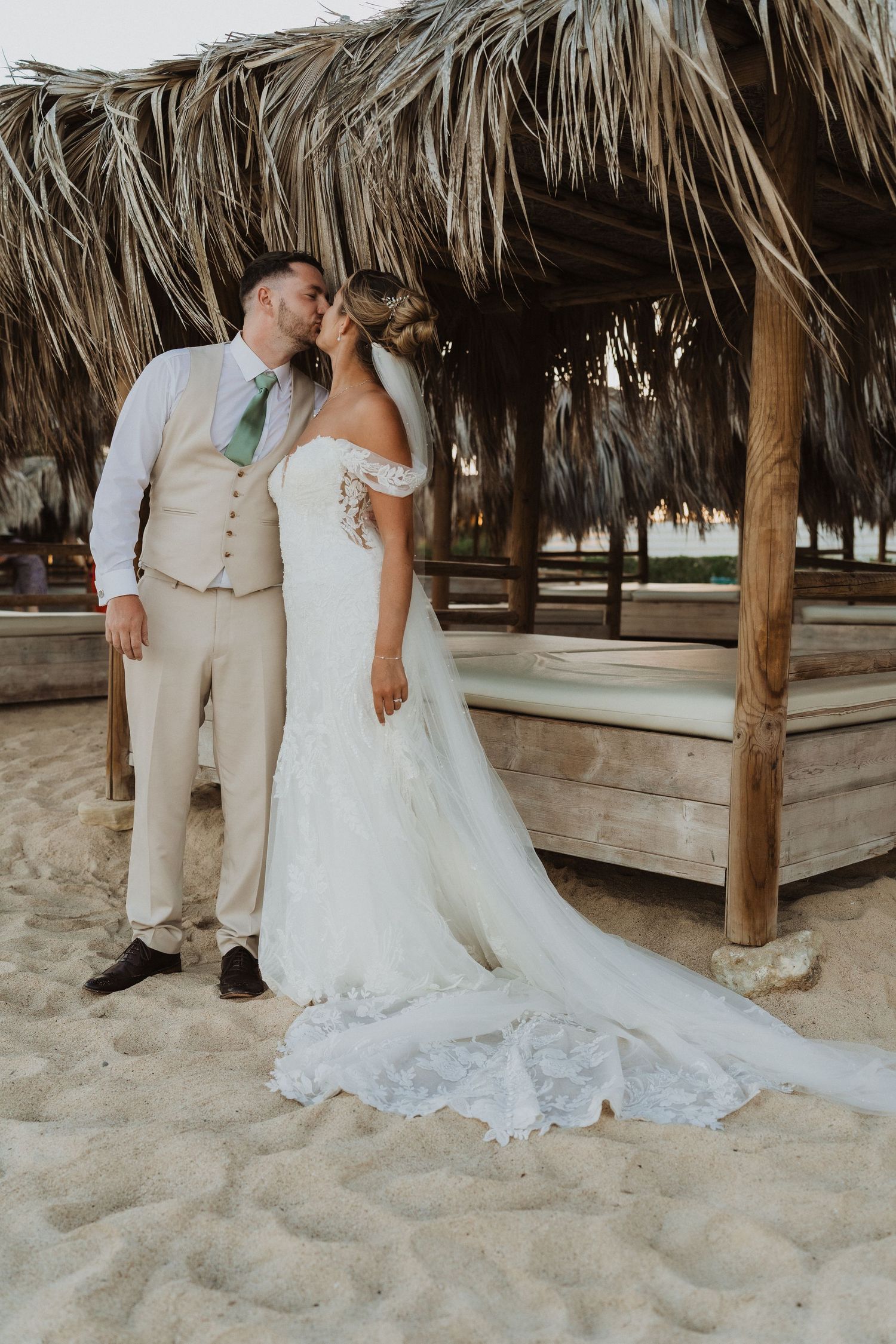 A couple shares a romantic moment under a thatched palapa on a sandy beach during their tropical wedding ceremony.