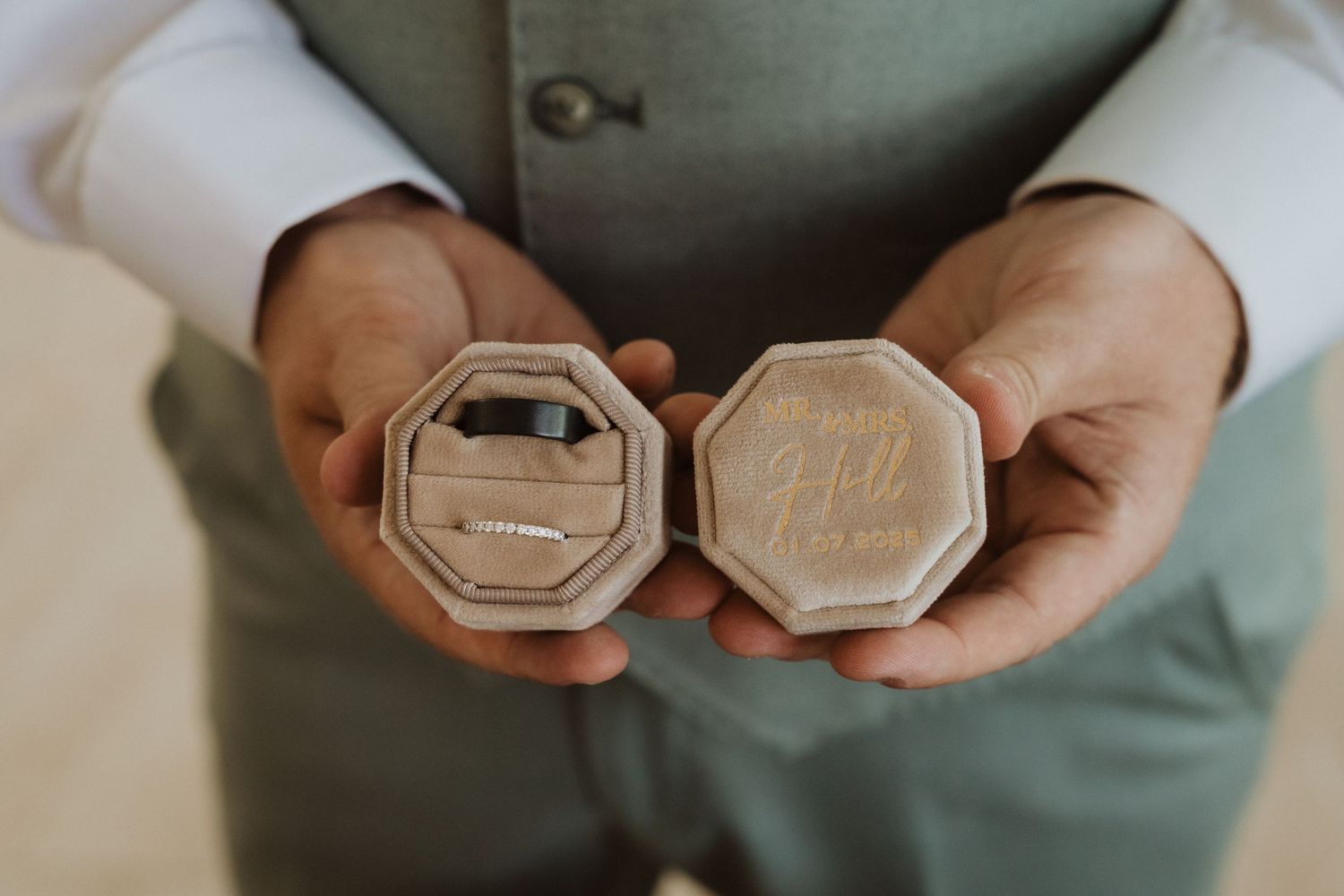 Close-up view of hands holding wedding rings against a neutral background.