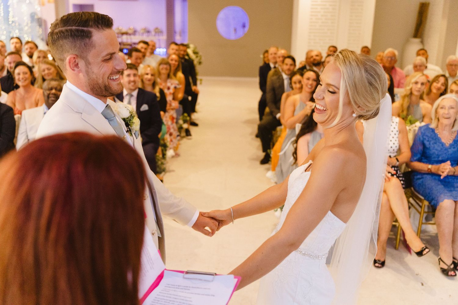 A candid moment during wedding vows with guests watching in the background.