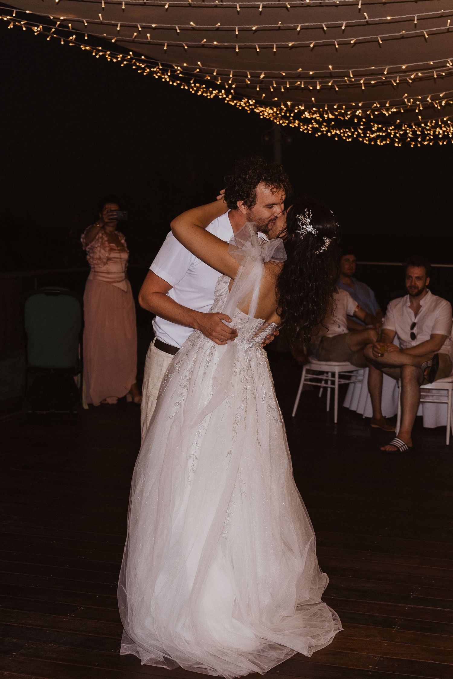A couple enjoys an intimate dance moment under glowing string lights at their wedding reception.