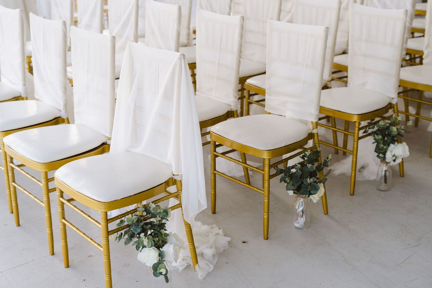 Elegant white chair covers with gold frames and floral decorations arranged for a formal event.
