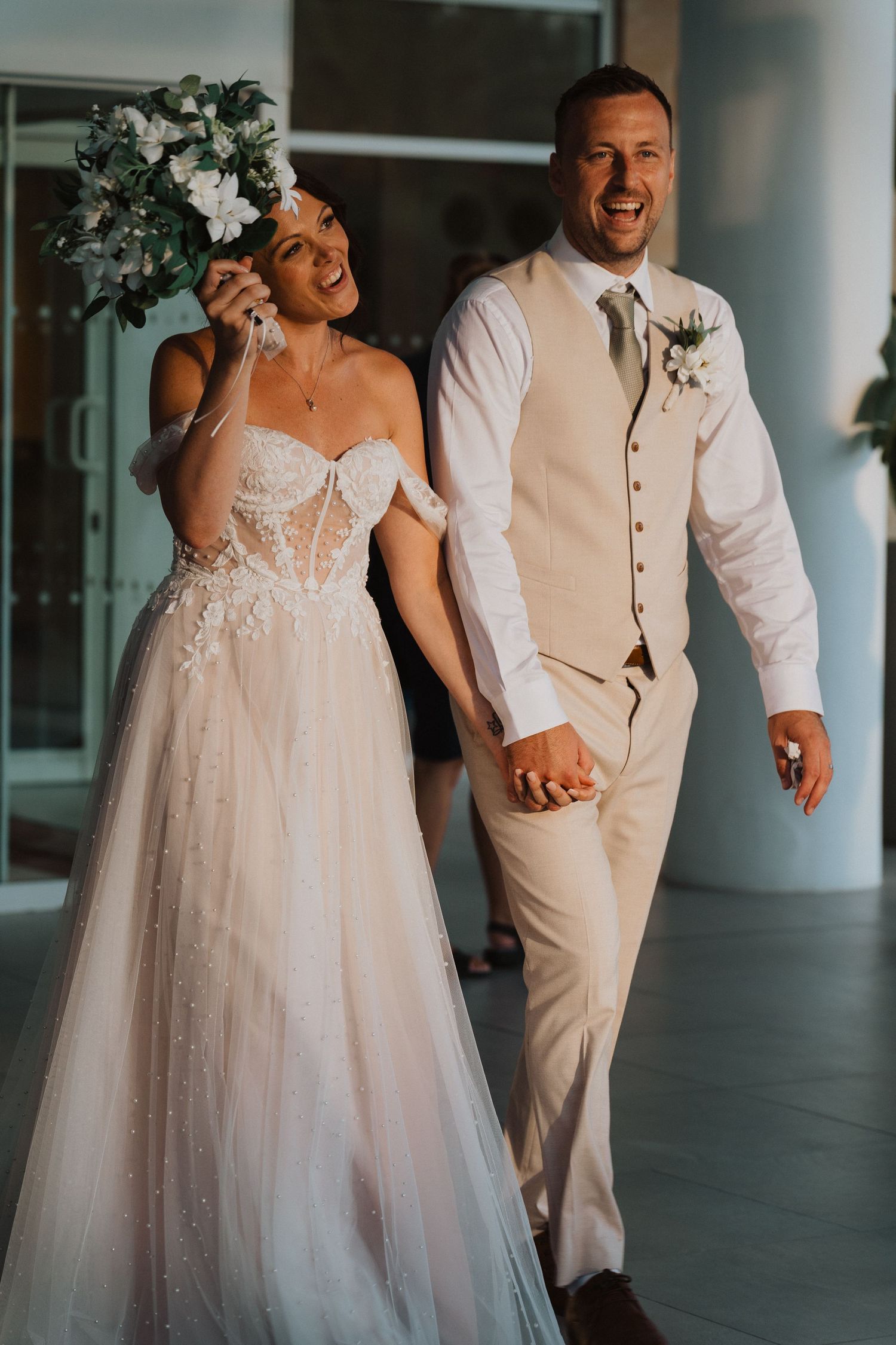 A happy couple sharing a joyful moment on their wedding day, with the bride in a sparkly tulle gown and groom in tan suit.