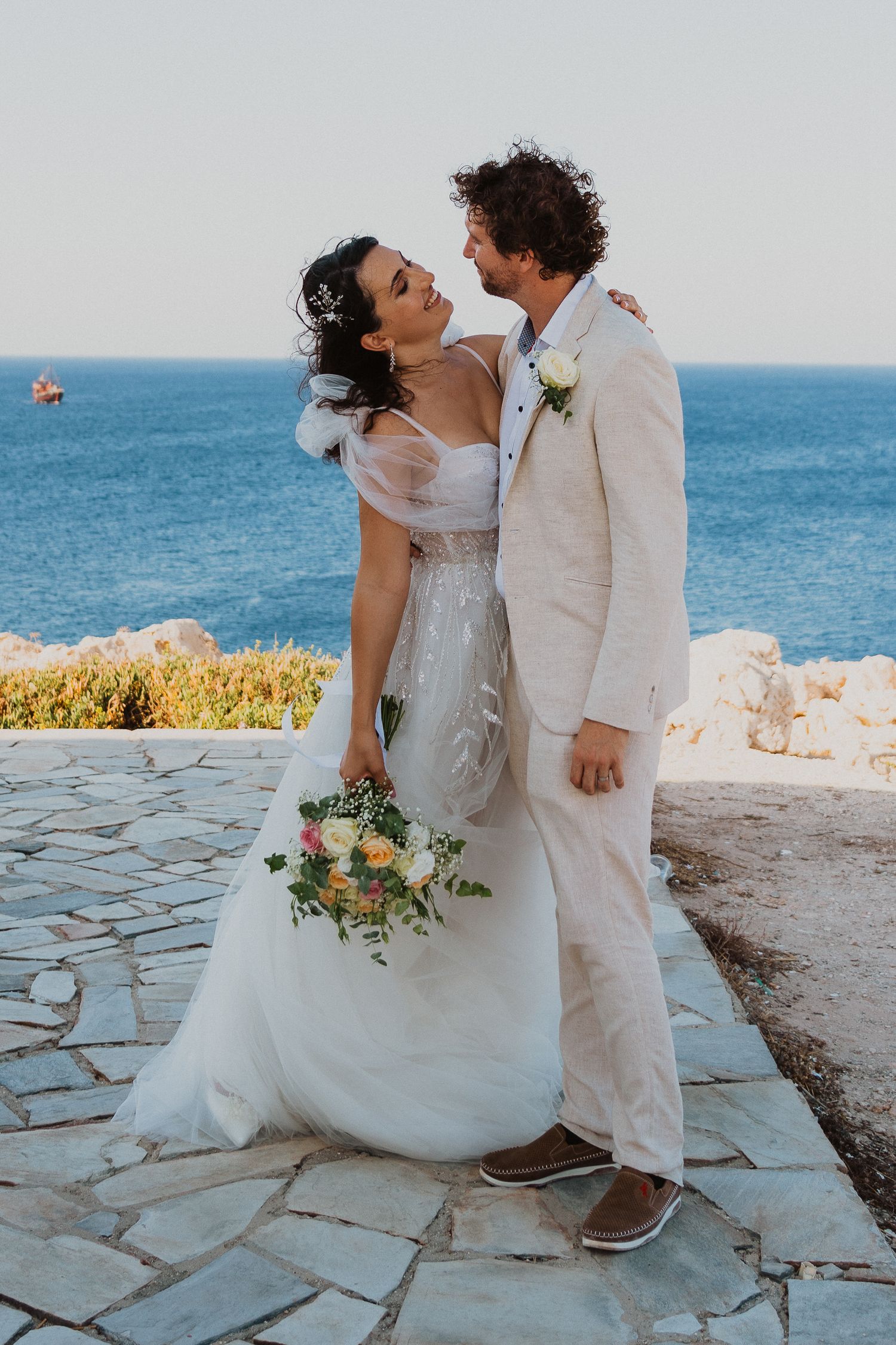 A newlywed couple shares a romantic moment on a stone terrace overlooking the Mediterranean Sea.