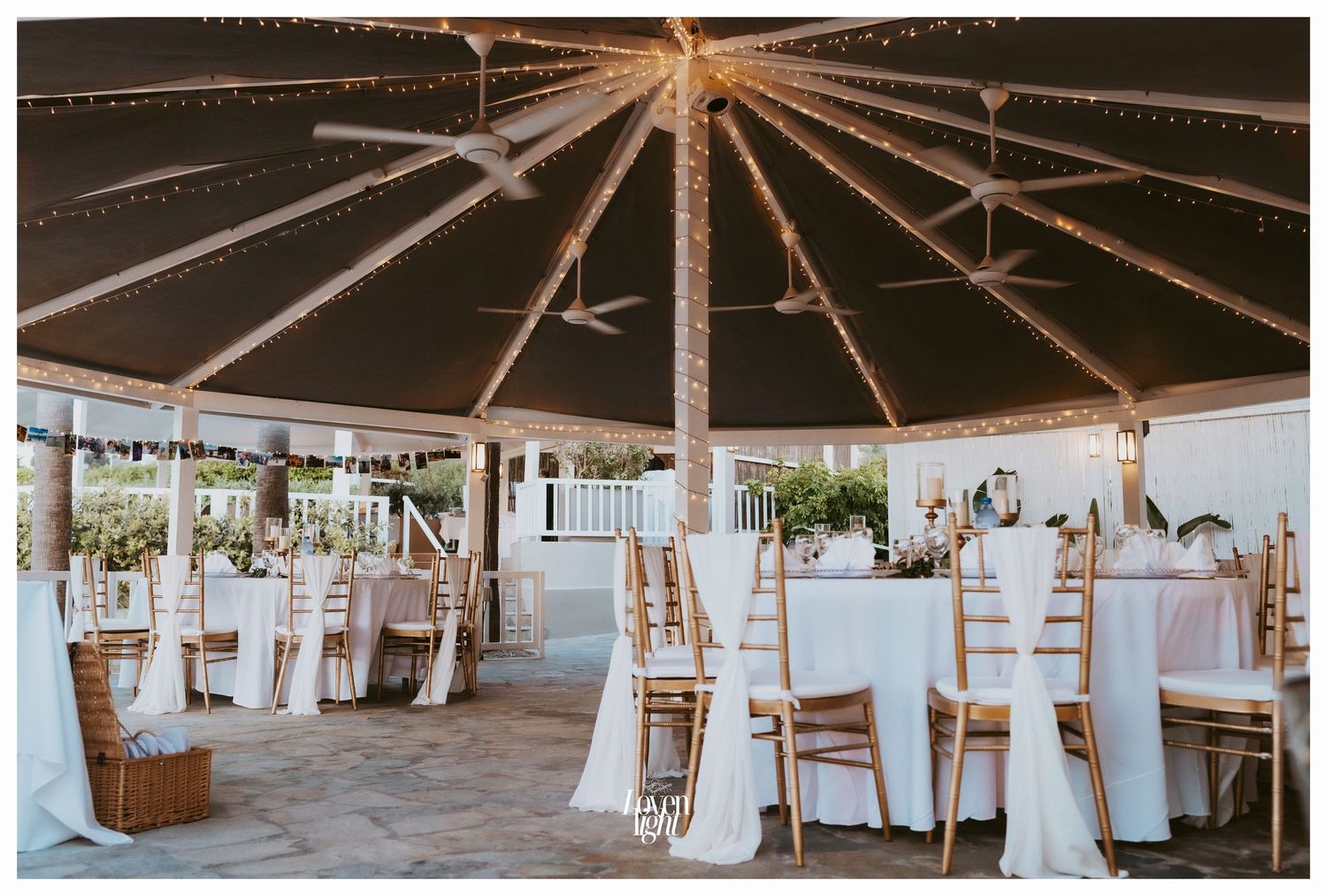 Wedding reception space with radial string lights and elegant table settings under a covered structure.