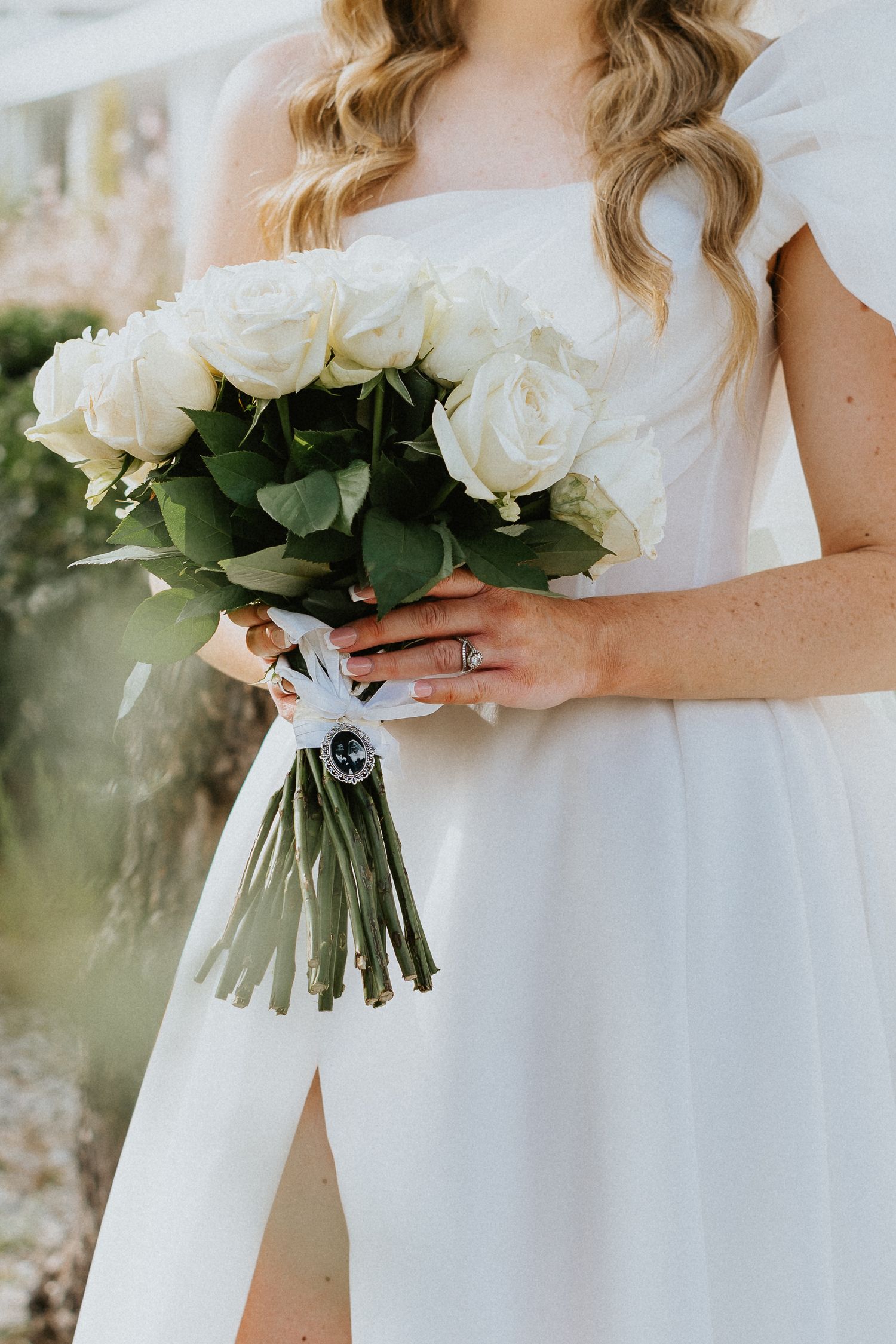 Close-up of bride holding classic white rose bouquet with flowing dress detail.