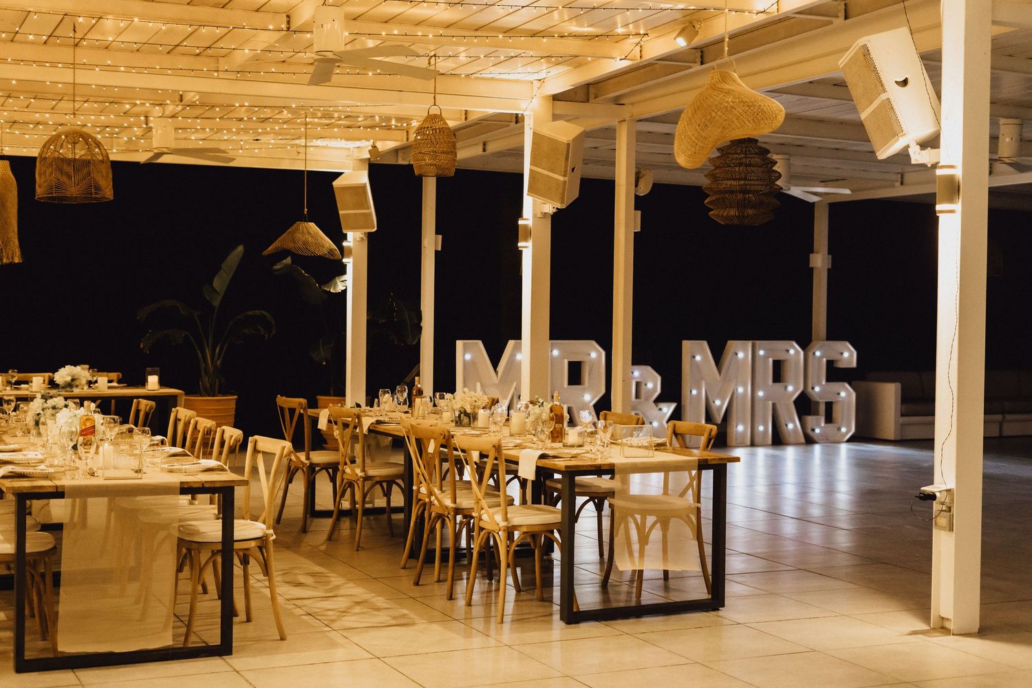 An elegant wedding reception venue setup with wooden tables and white pillars.