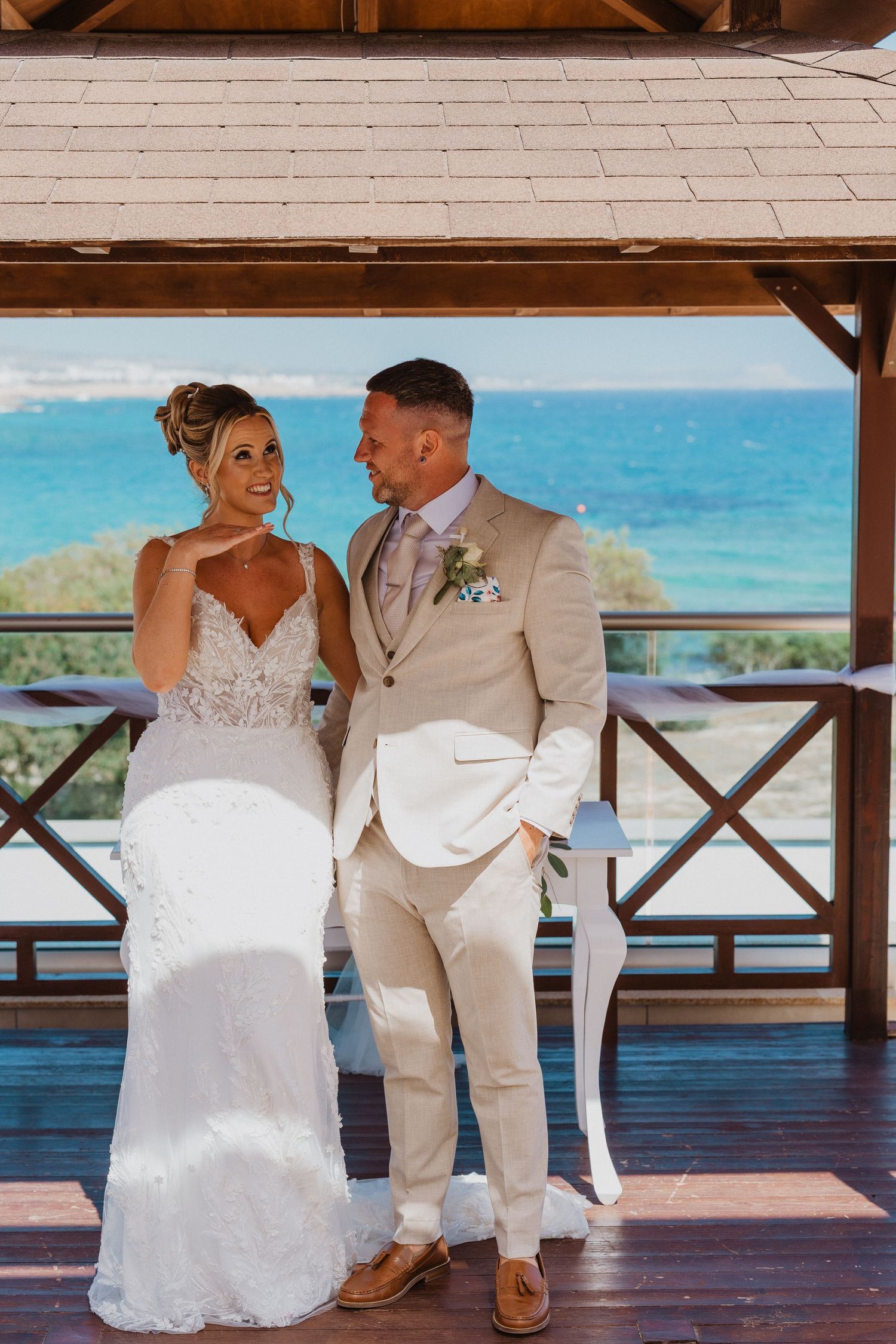 A romantic wedding photoshoot series showing a couple sitting together on a deck overlooking turquoise ocean waters.
