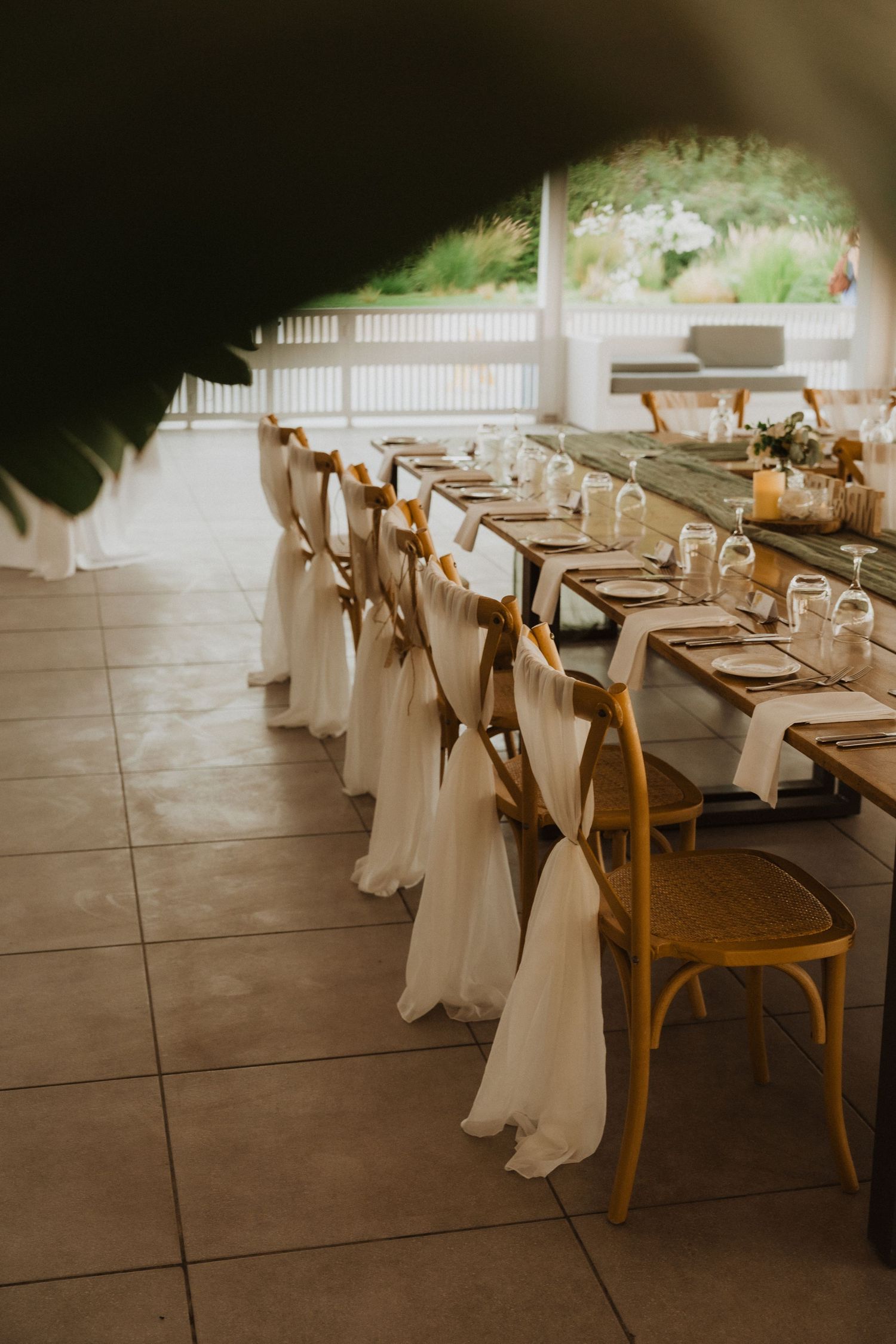 Elegant dining setup with wooden chairs draped in flowing white fabric and rustic table settings.