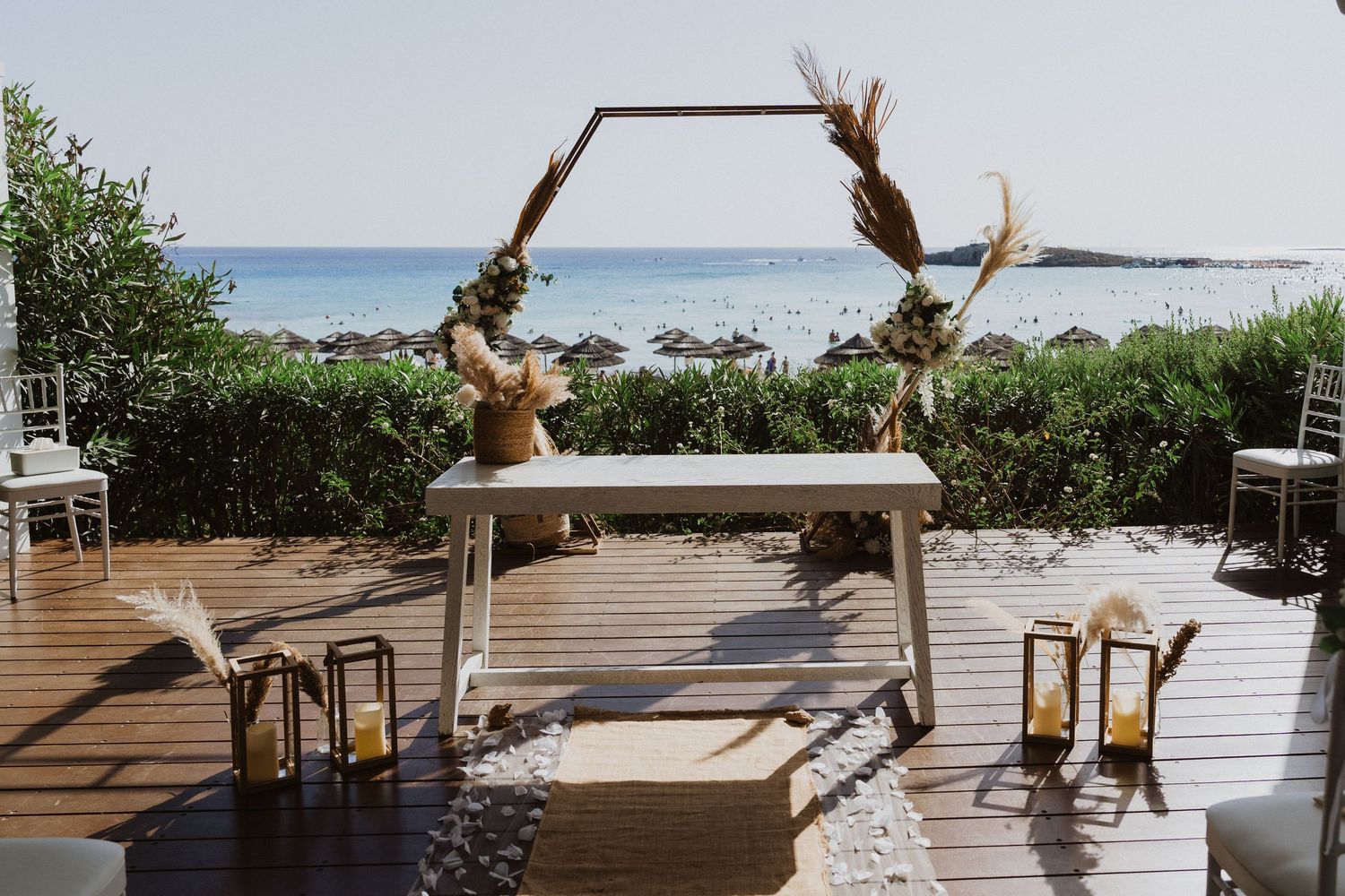 Wedding ceremony setup with wooden arch and lanterns overlooking Mediterranean waters.
