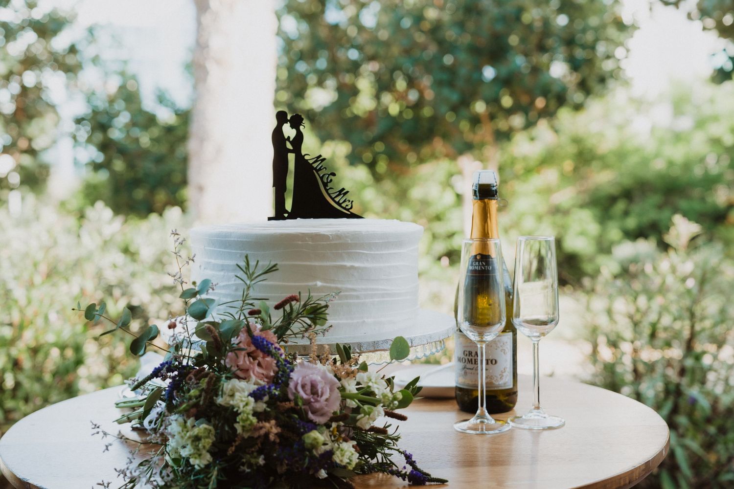Wedding reception table with floral arrangements and champagne in outdoor setting.