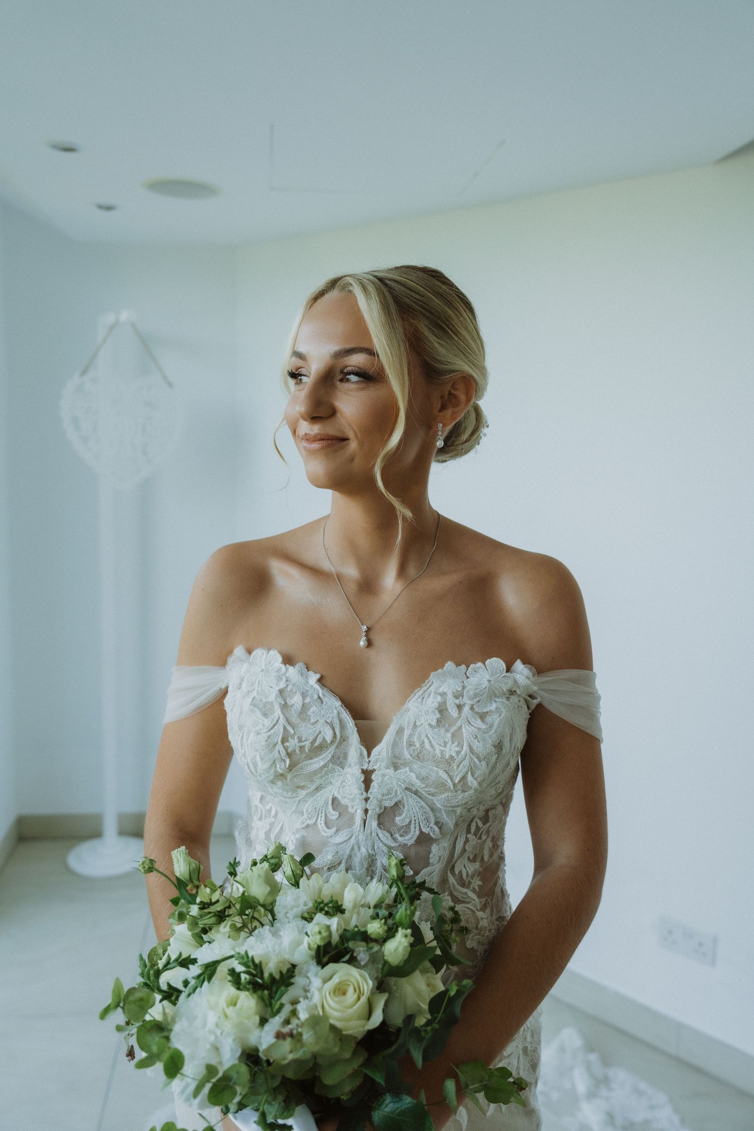 Bride holding a white and green wedding bouquet in an off-shoulder lace gown.