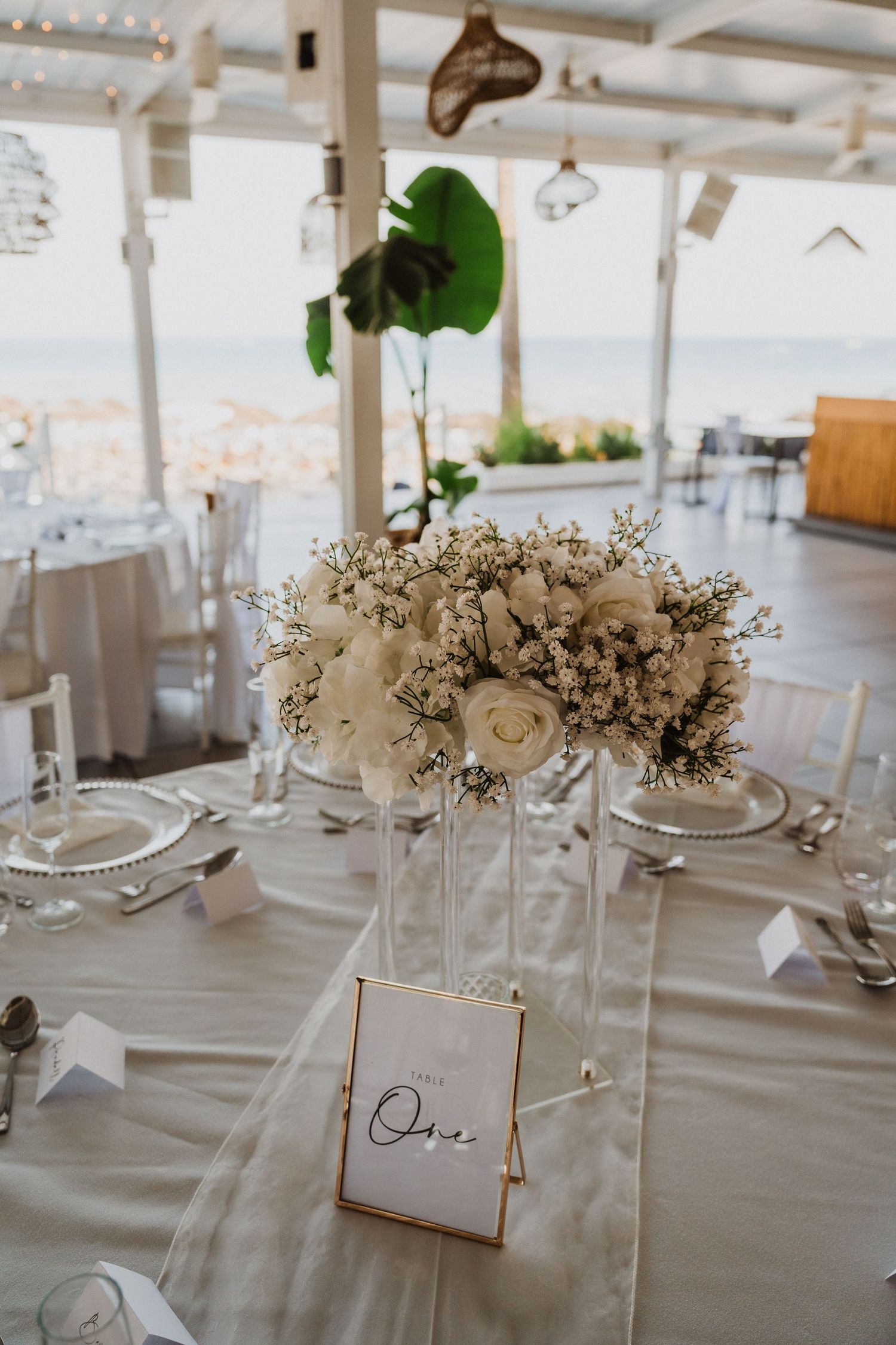 Elegant wedding reception tables decorated with white floral centerpieces and place cards in a bright coastal venue.