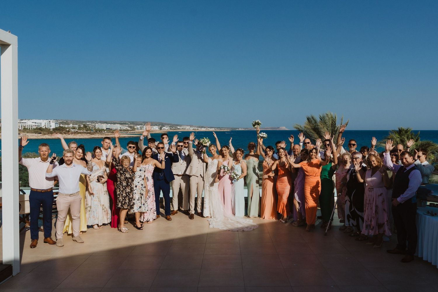 Wedding guests celebrate on an outdoor terrace with ocean views.