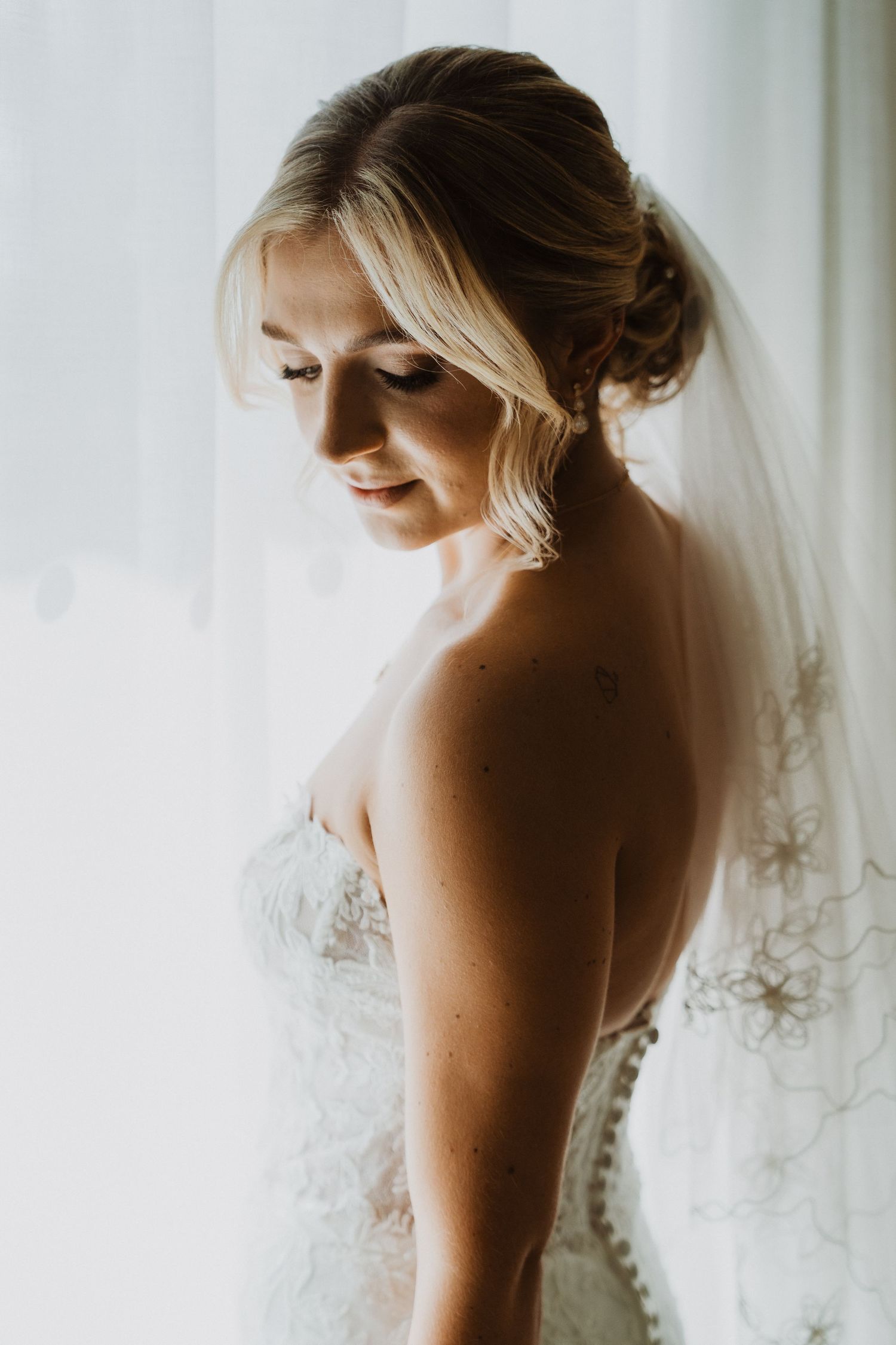 Ethereal bridal portrait showing intricate lace details and delicate veil against white curtains.