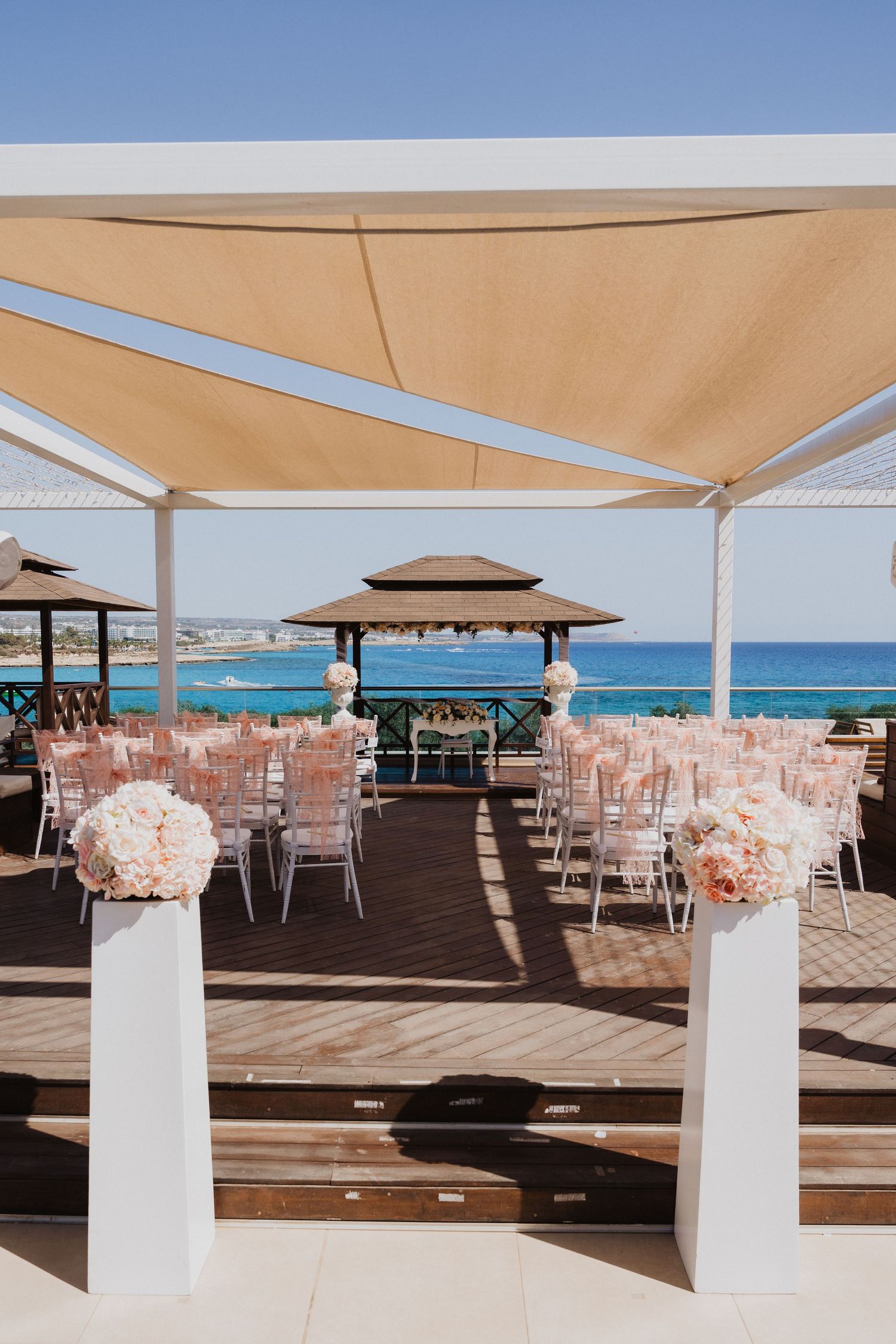 Beachfront wedding venue with white columns and tan canopy overlooking blue ocean.