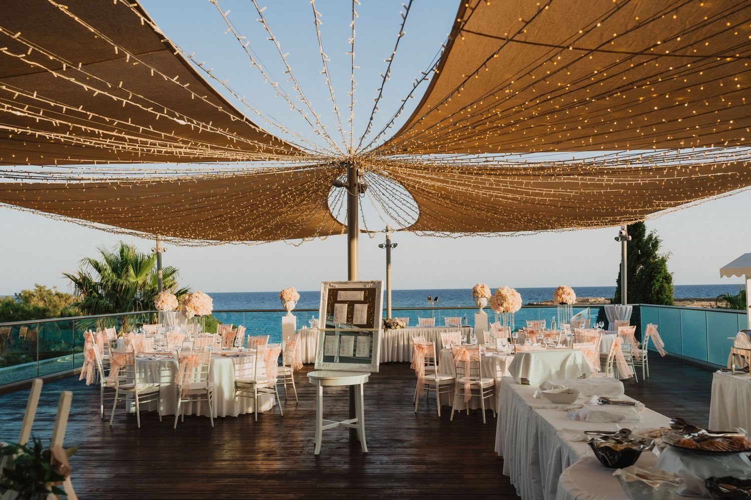 Beach wedding reception setup with fairy lights and brown sail shades creating an intimate atmosphere.