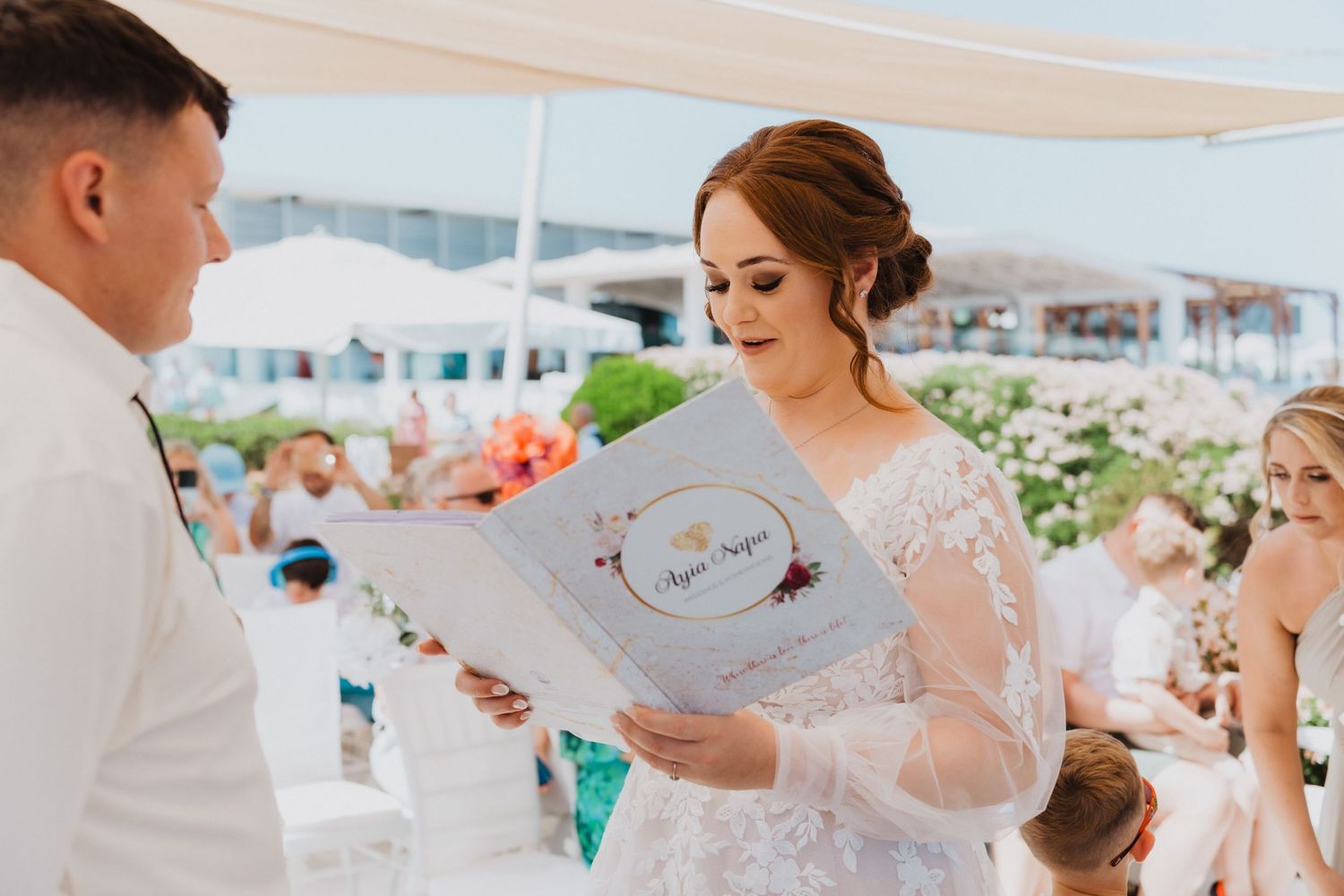 A couple exchanges wedding vows during a beachside ceremony with guests watching.