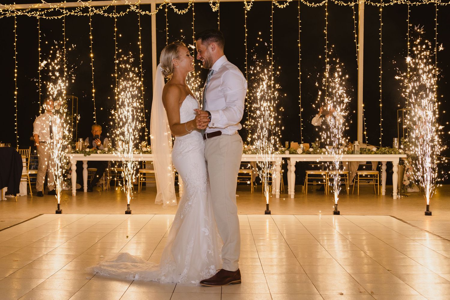 Romantic wedding dance captured with warm lighting and dramatic sparkler fountains behind the couple.