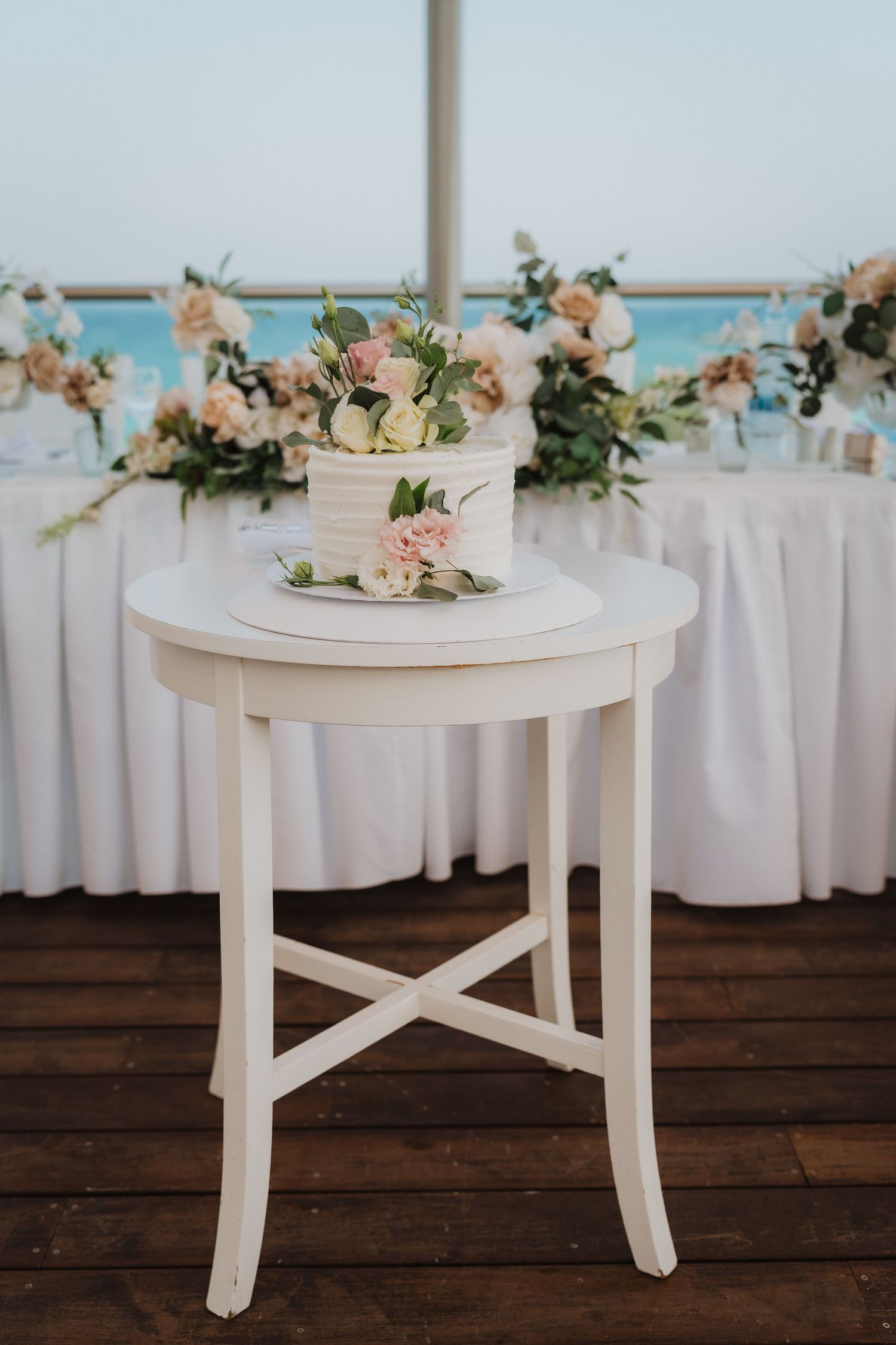 Single tier white wedding cake with floral decorations displayed on white round accent table.