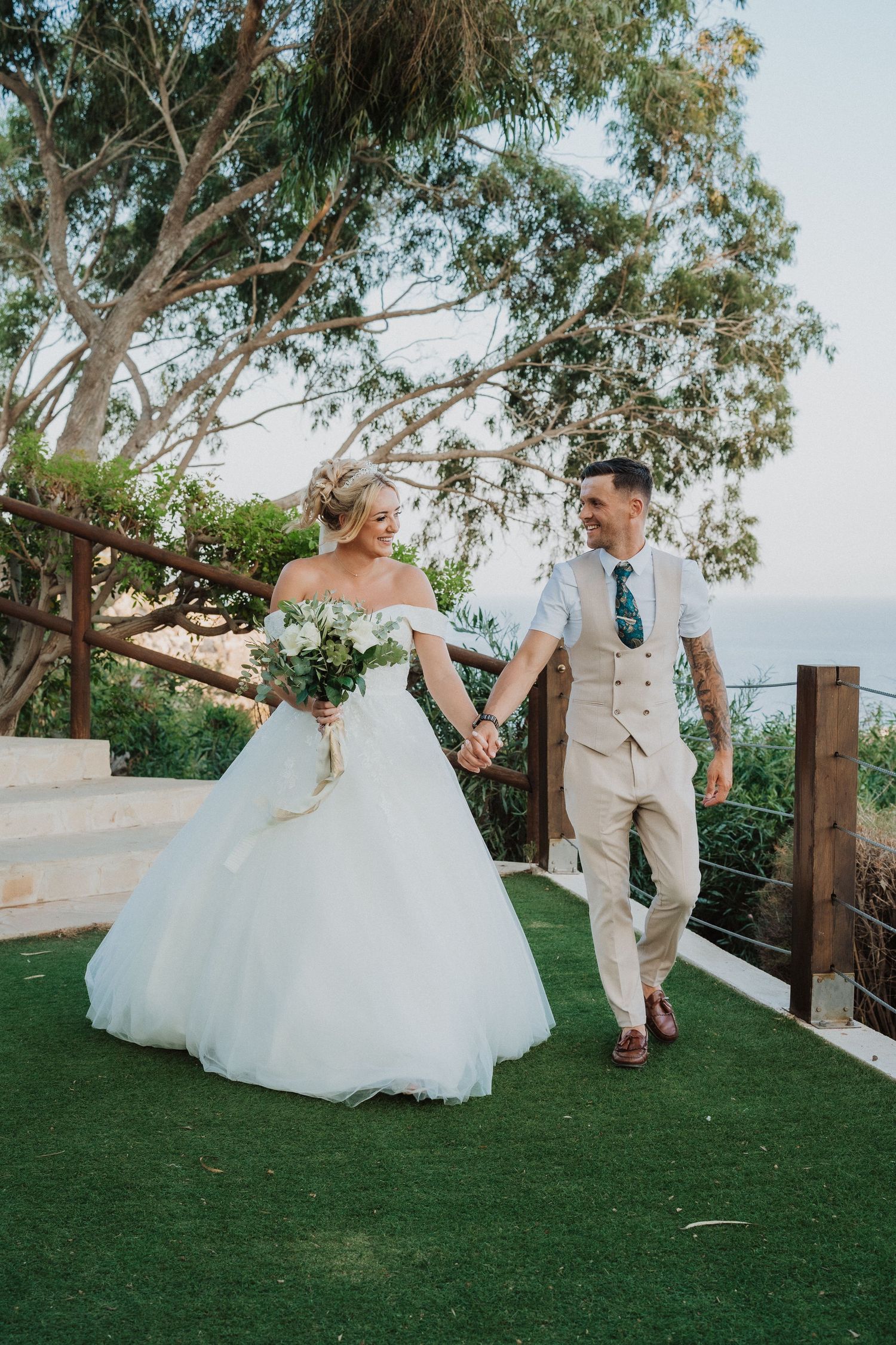 A couple walks hand in hand on an outdoor terrace with eucalyptus trees and mountain views in the background.