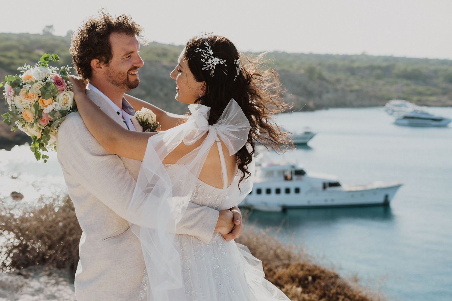 A candid moment of laughter and love between newlyweds on a scenic coastal cliff.