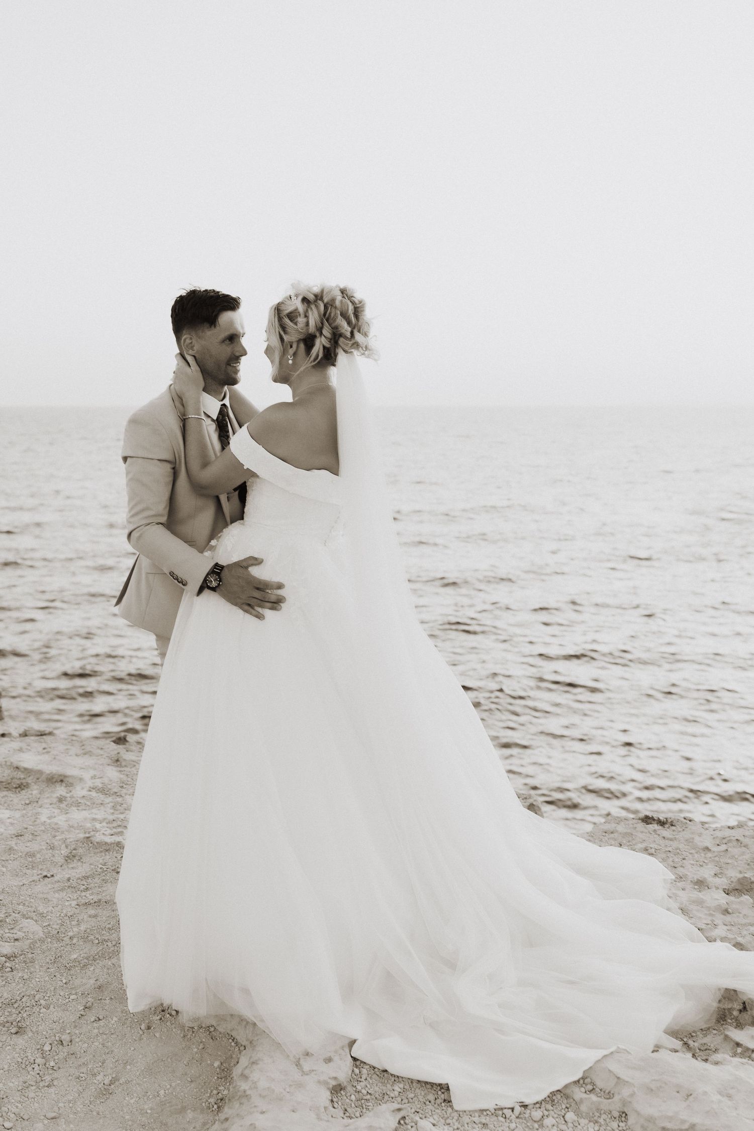 A romantic black and white beach wedding portrait with flowing white dress and beige suit.