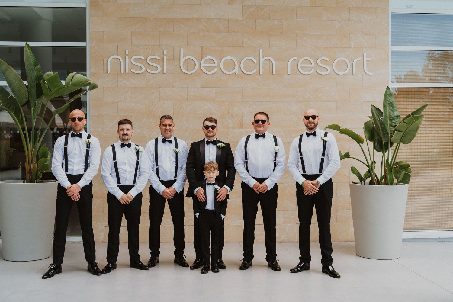 Groomsmen in formal attire posing outside Nissi Beach Resort.