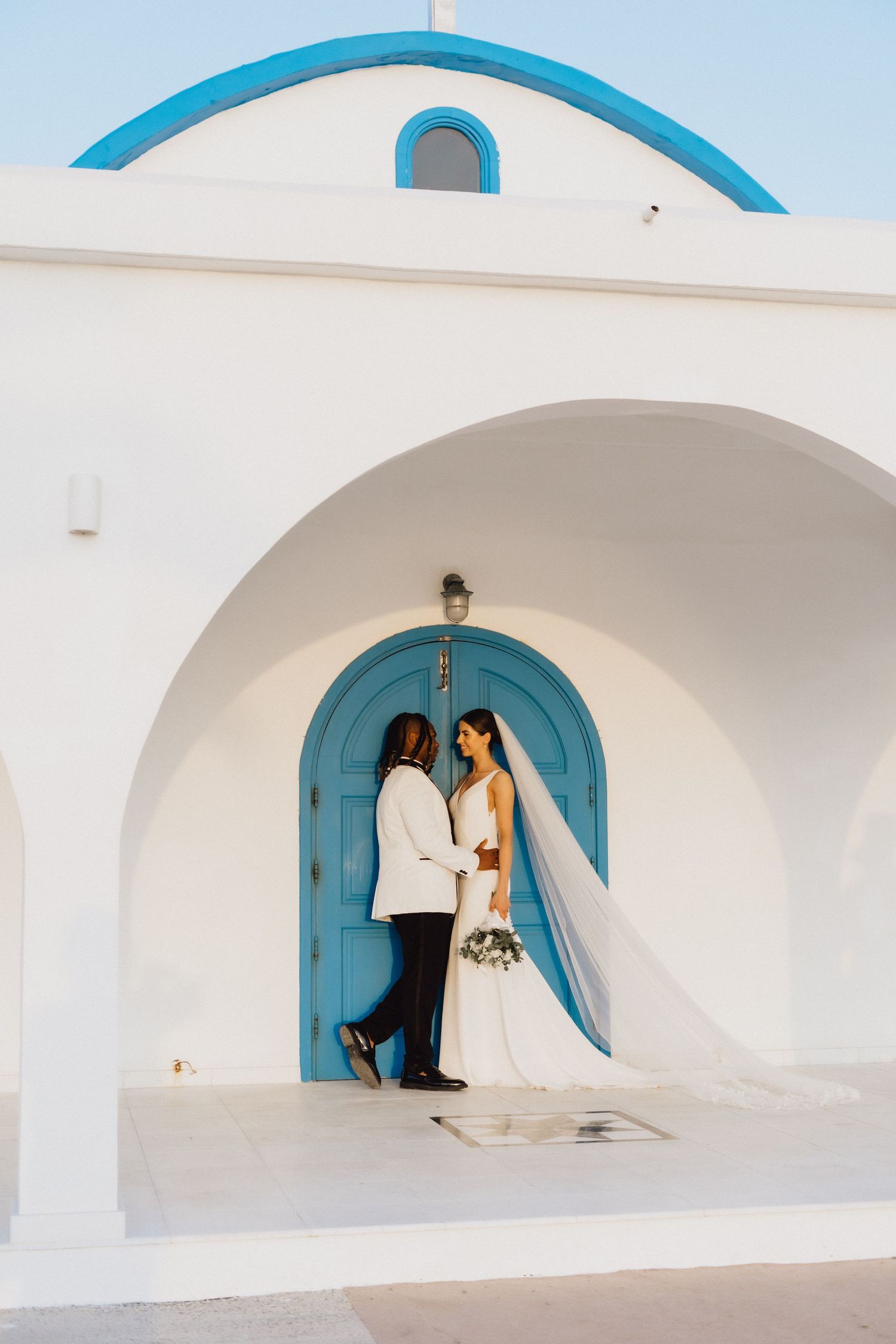 A wedding couple stands before a bright turquoise door in classic Mediterranean architecture.