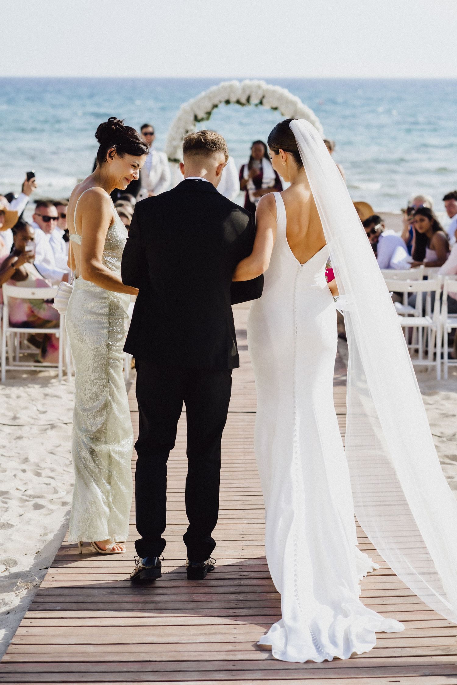 A beach wedding ceremony in progress on a wooden boardwalk with ocean views.