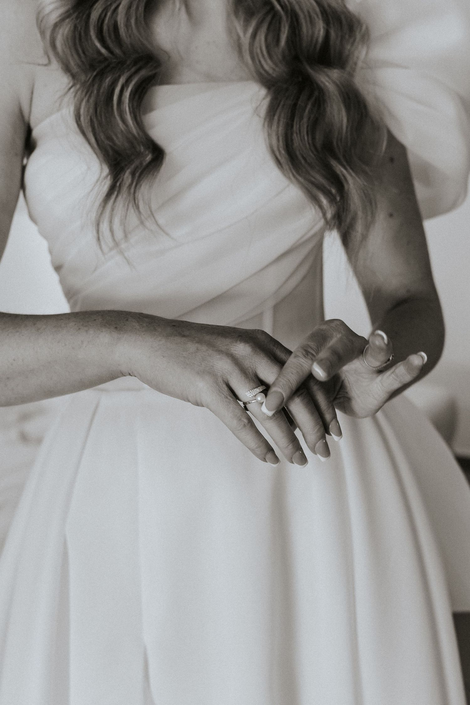 Close-up detail of a white wedding dress and clasped hands.