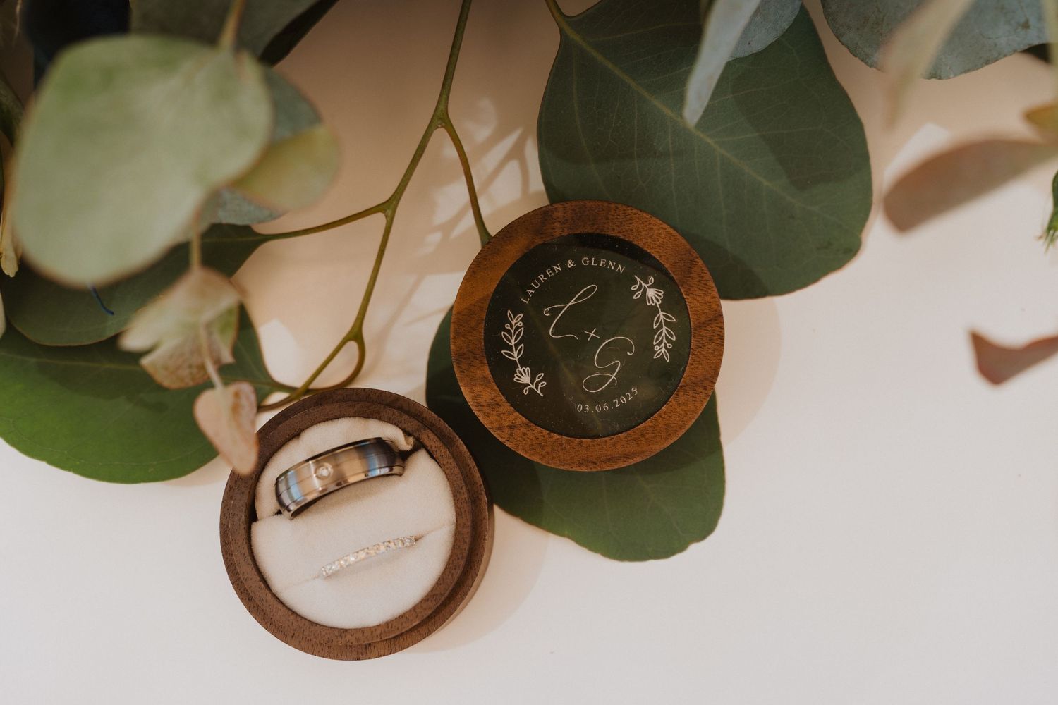 Wedding rings and eucalyptus leaves arranged on a rustic wooden surface.