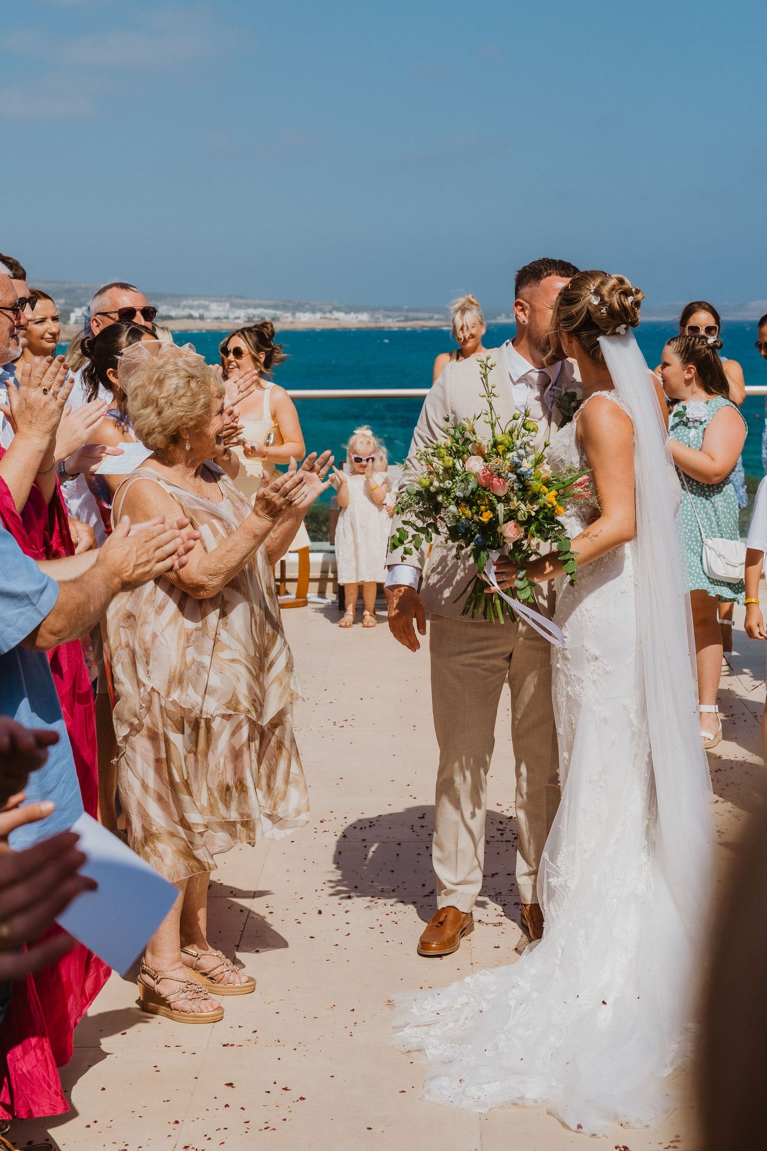Beach wedding ceremony with guests celebrating on sandy shore as turquoise ocean waves roll in the background.