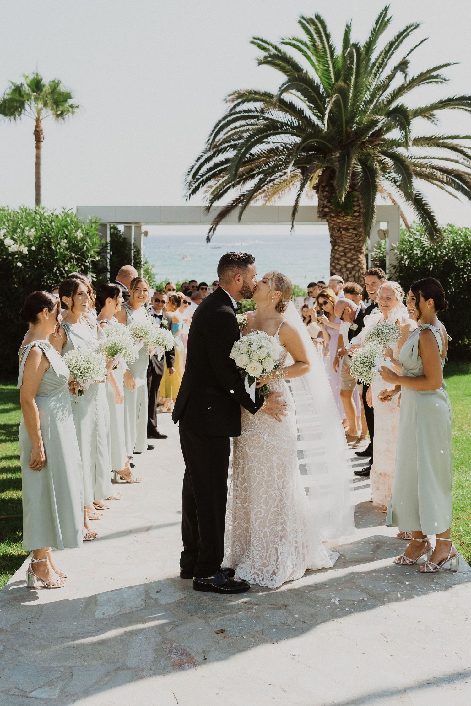 Wedding celebration lineup on a sunny terrace with tropical palm trees and coastal views.